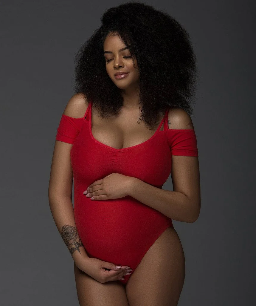 Chicago Maternity Photography showing a pregnant mom wearing a red bodysuit and cradling her belly