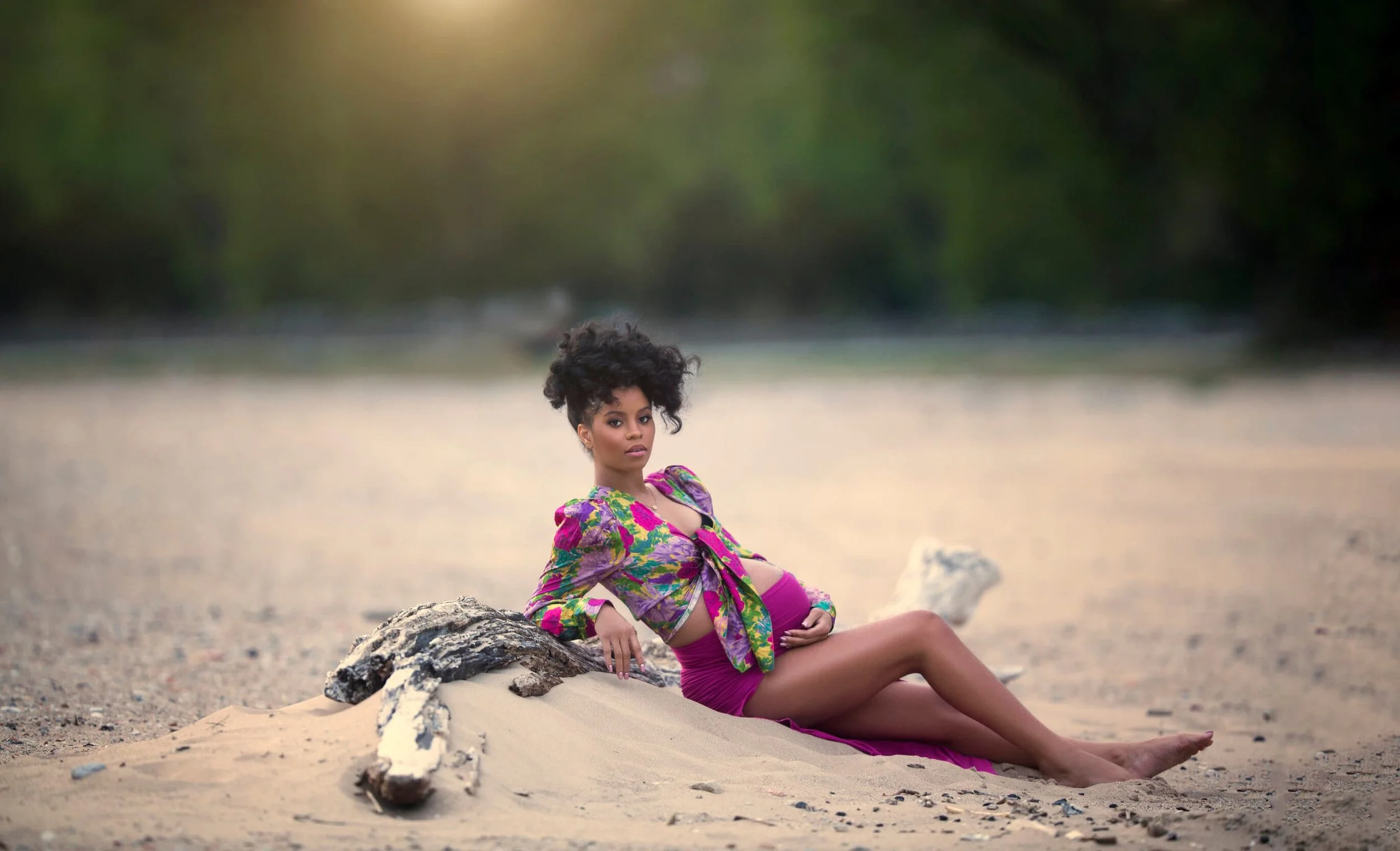 A pregnant Chicago woman with dark curly hair sitting on Southshore Lake Michigan beach wearing a colorful purple dress
