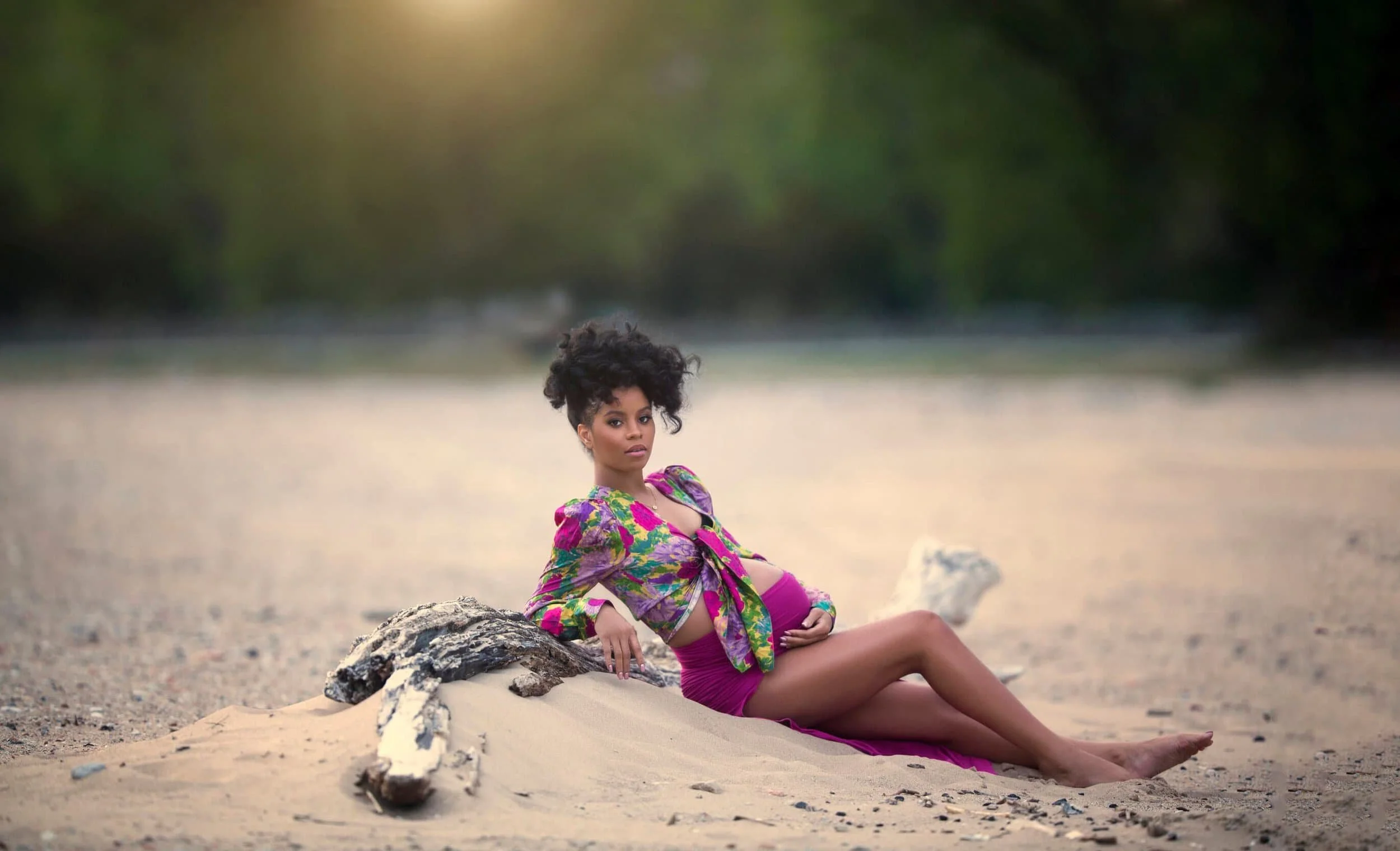 A pregnant Chicago woman with dark curly hair sitting on Southshore Lake Michigan beach wearing a colorful purple dress