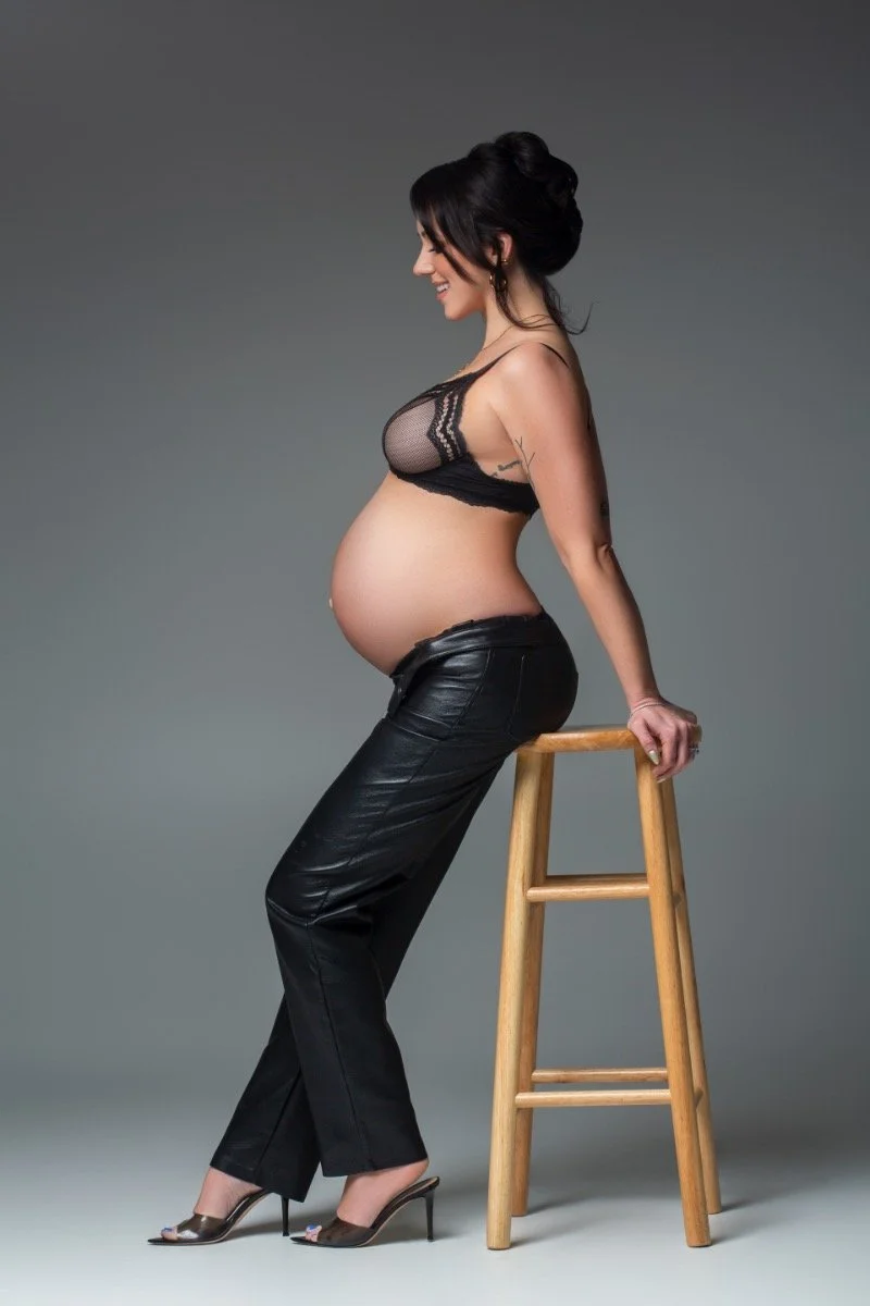 Stunning side-profile maternity portrait of a pregnant woman in elegant black lace bra and leather pants, captured in studio by Chicago maternity photographer Sri and Jana Photography