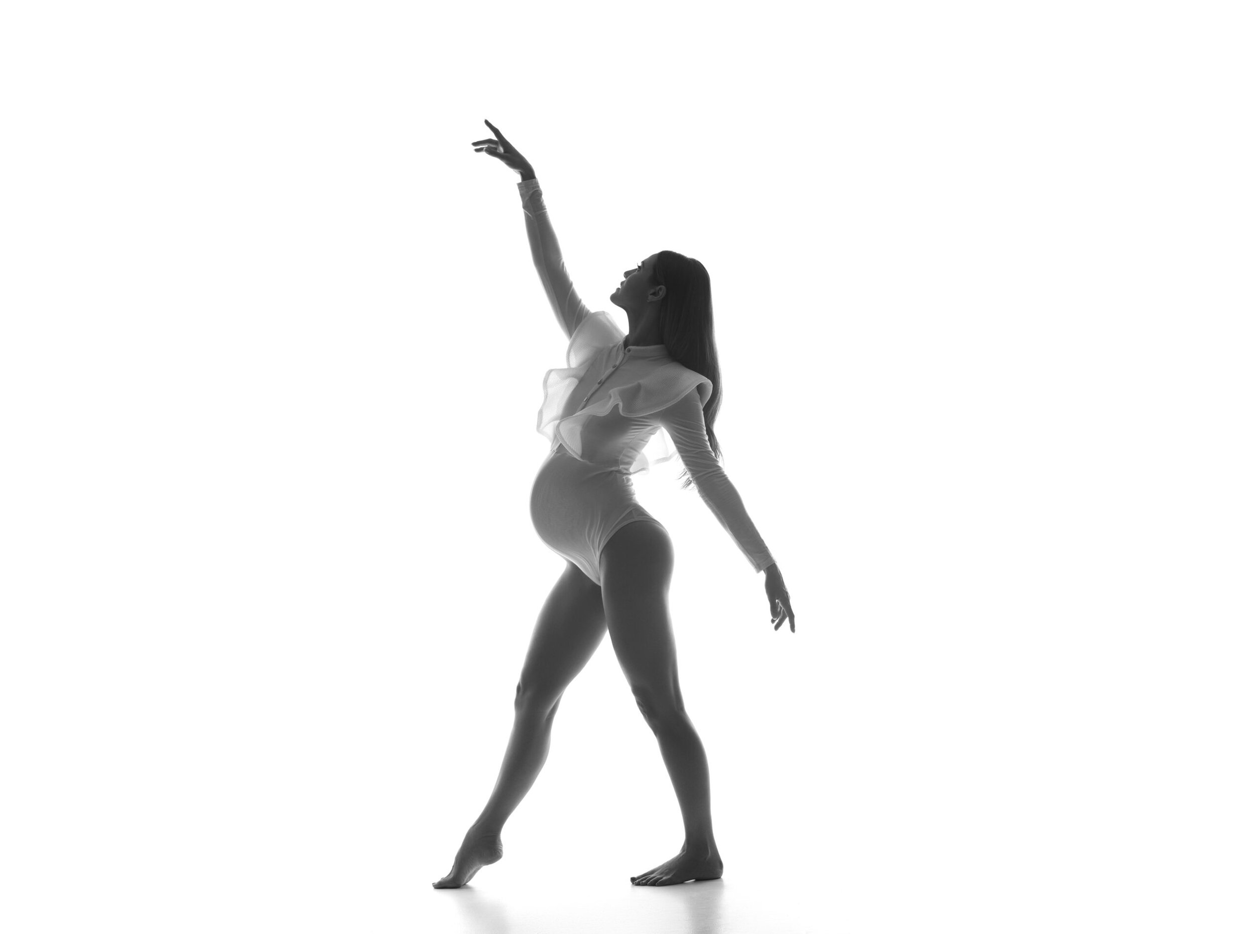 Chicago maternity photographer high-key studio portrait of pregnant woman in sheer white bodysuit.