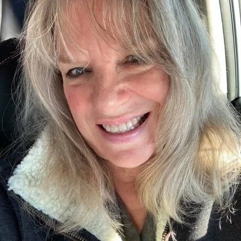 Close-up of a woman smiling with blonde hair and a fur-lined jacket.