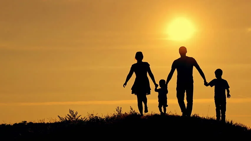Silhouette of four people, two taller and two shorter, holding hands and walking into a sunset.