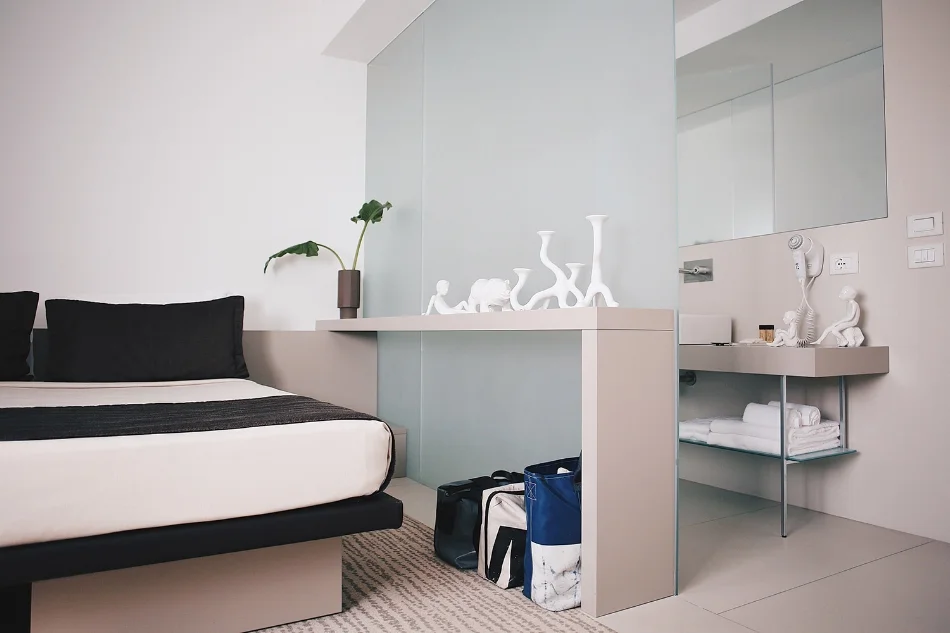Disponibile anche con letti separati, la camera doppia si distingue per eleganza e comfort. Una lastra di vetro opalino separa la camera da letto dall’ambiente che ospita la doccia e il lavabo, consentendo alla luce naturale di diffondersi e ai riflessi di moltiplicarsi.