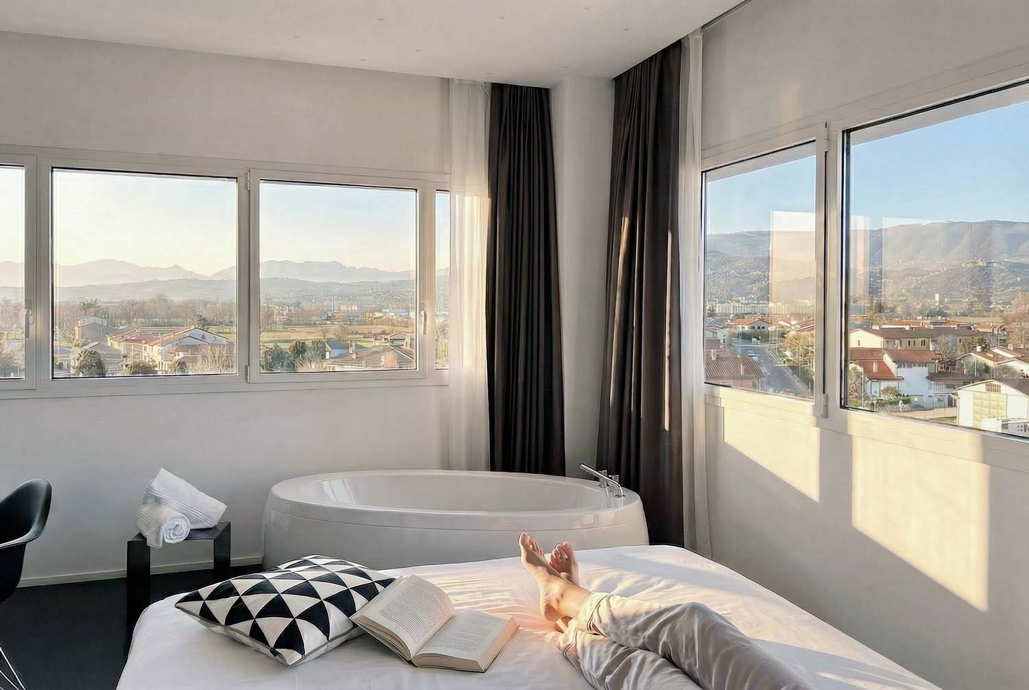  La  Panorama Suite , situata al quarto piano dell’hotel, si distingue per un’ampia finestra a nastro che corre su due pareti, aprendo lo sguardo su una vista davvero straordinaria. La vasca da bagno in camera, l’eleganza degli arredi e il paesaggio 