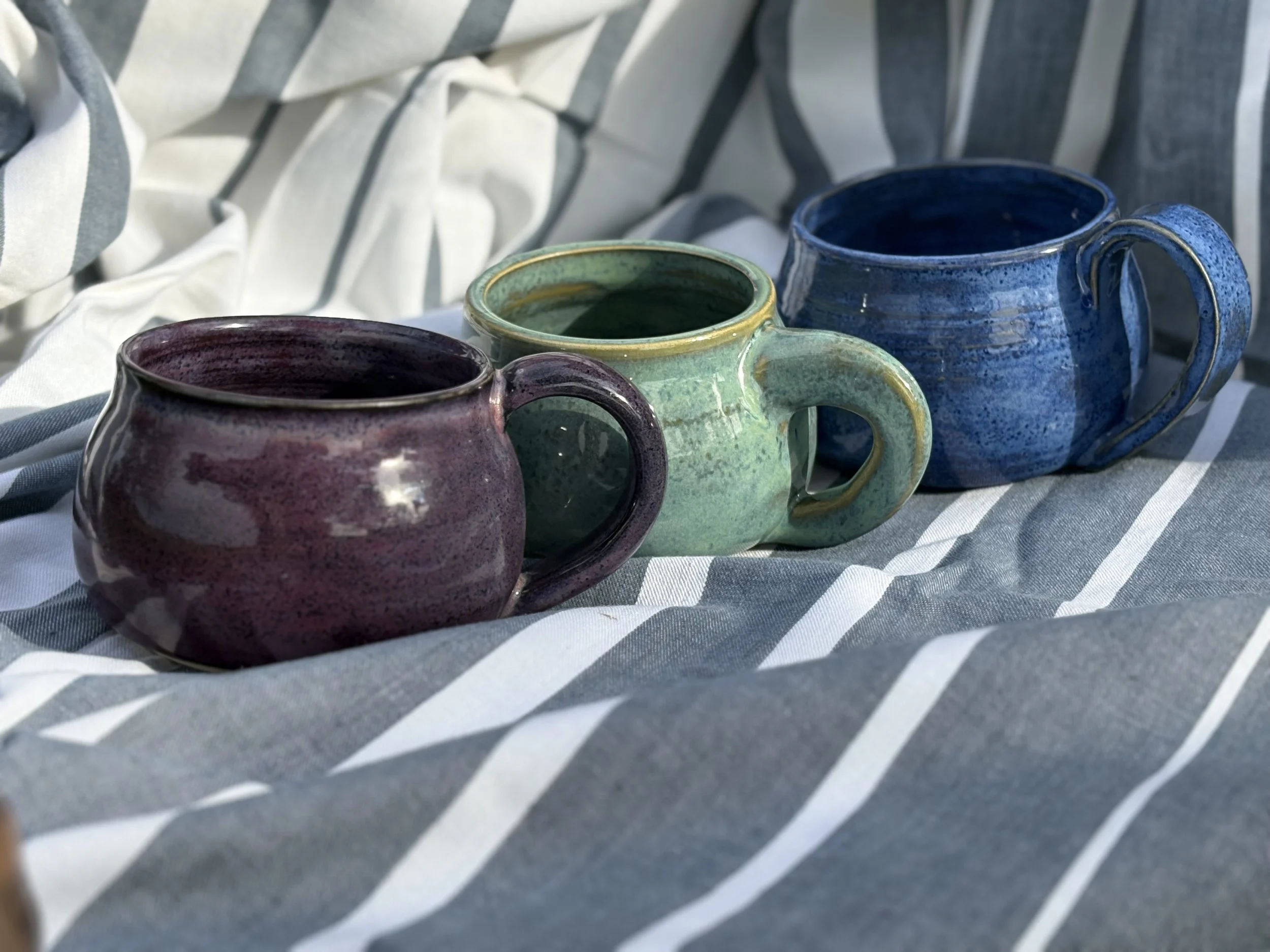 one each: a purple, green and blue coffee mug lined up with handles facing the same direction