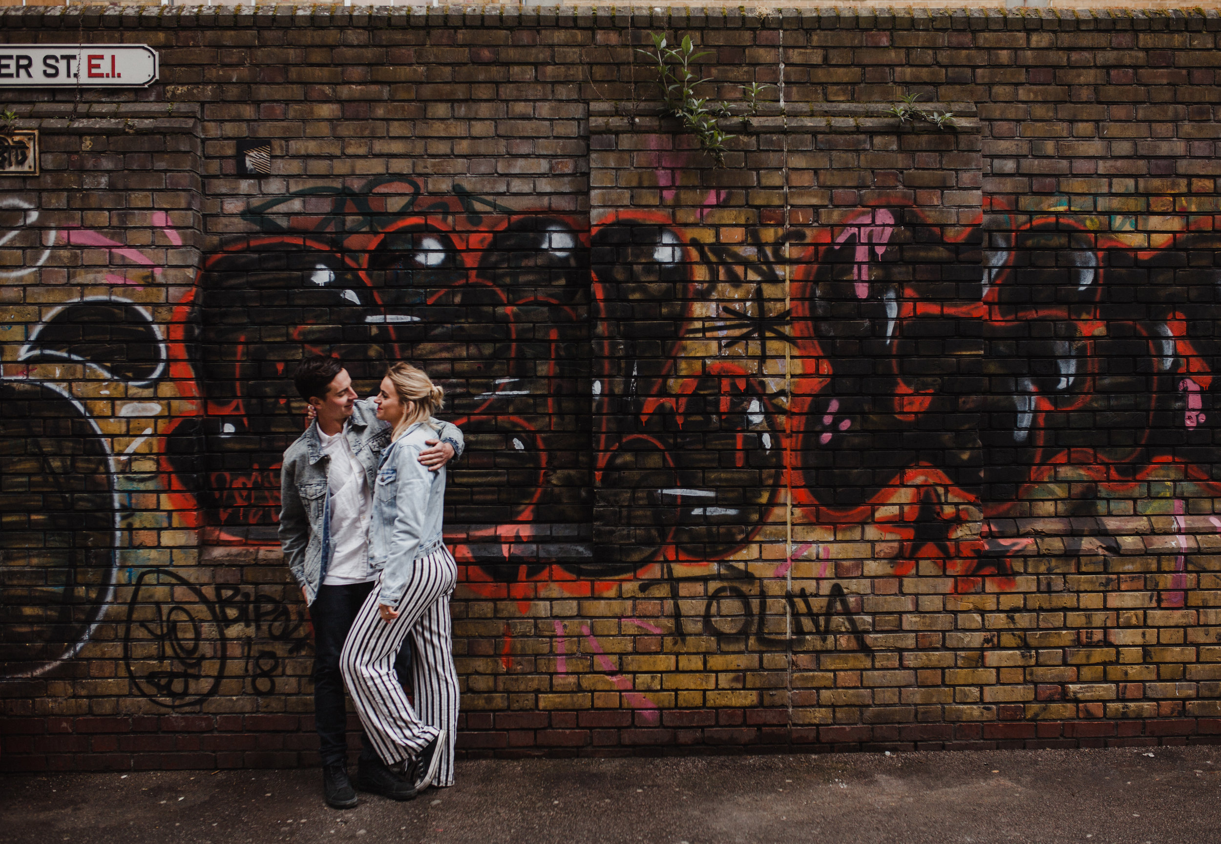 A natural style portrait of couple embracing with a graffiti backdrop.