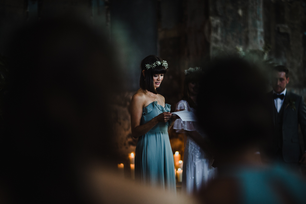 The bridesmaid delivers a reading in candle light during the wedding ceremony.