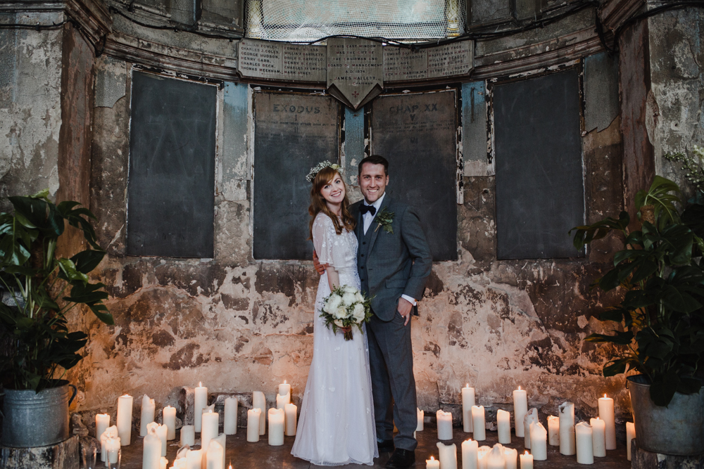 Bride and groom pose for a portrait surrounded by candles in the Asylum Chapel.