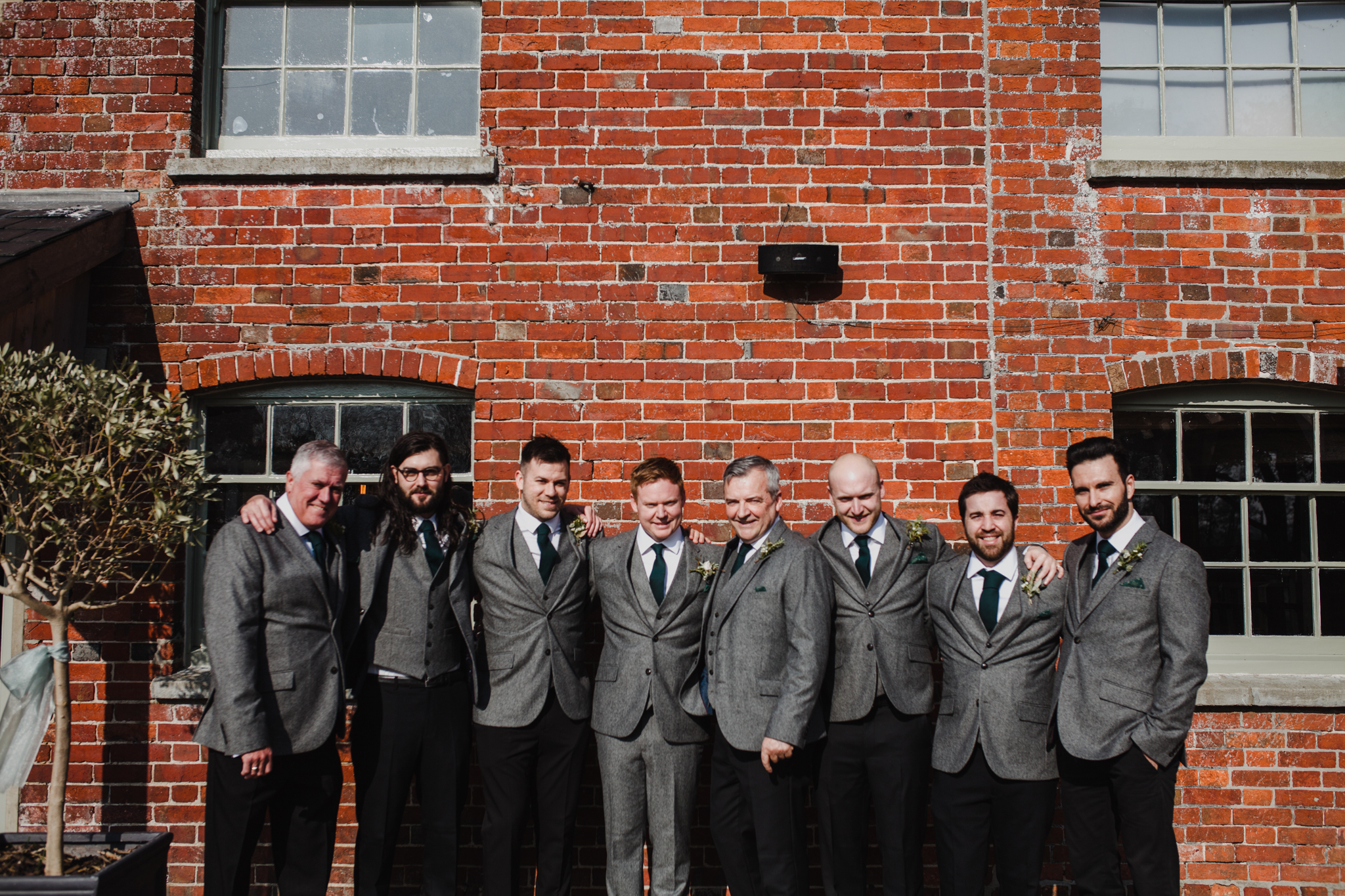 Groom and his ushers smiling in front of a brick wall