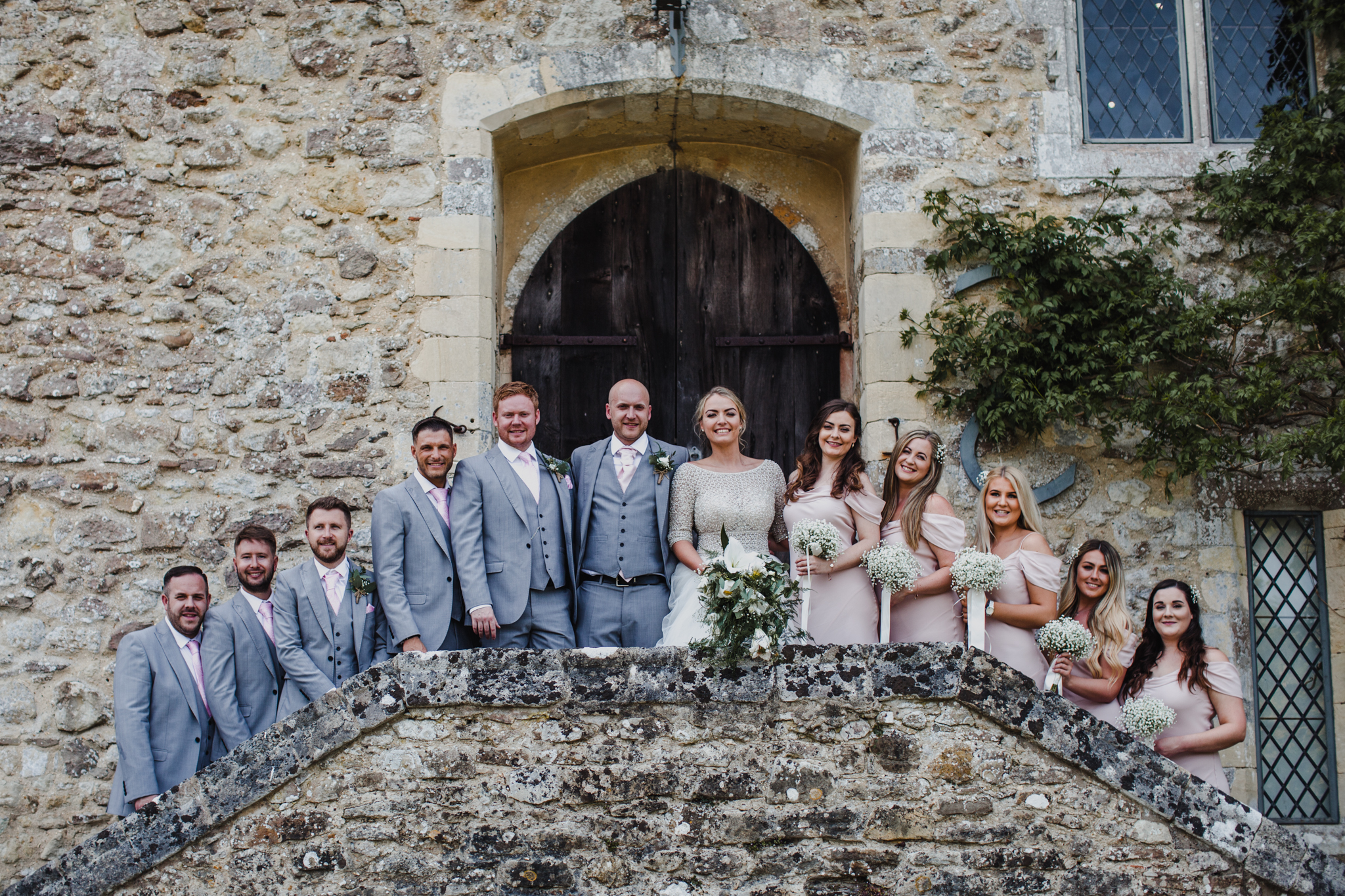 Bridal party lined up smiling in front of stone wall venue on stairs