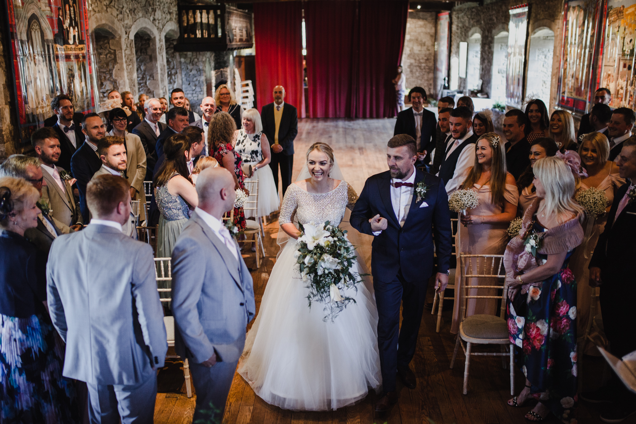 A bride and her father walking down the aisle in a dark castle style venue