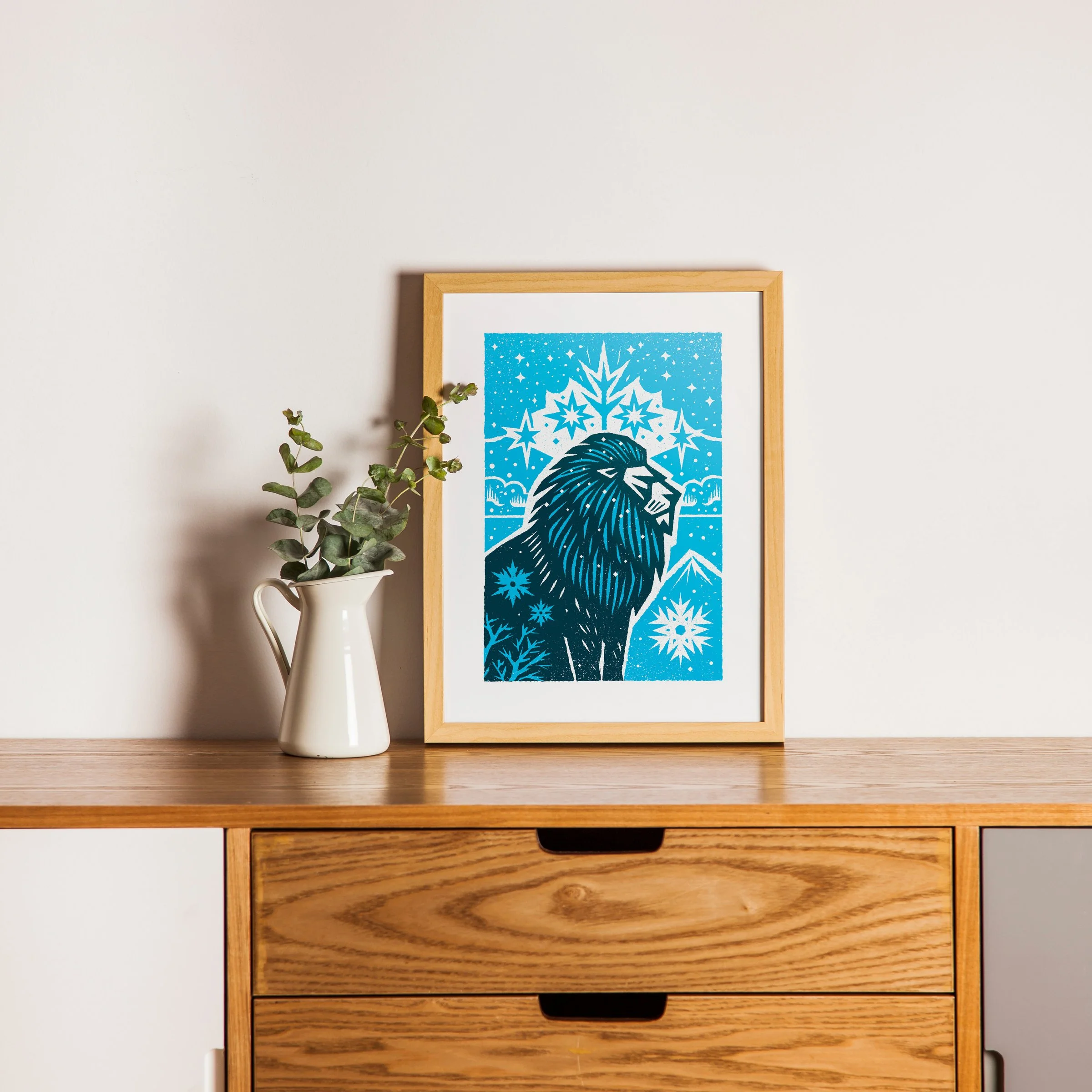 Maneful of Snow - Winter Lion Art Print, shown in a oak frame above an oak cabinet. Print supplied unframed.