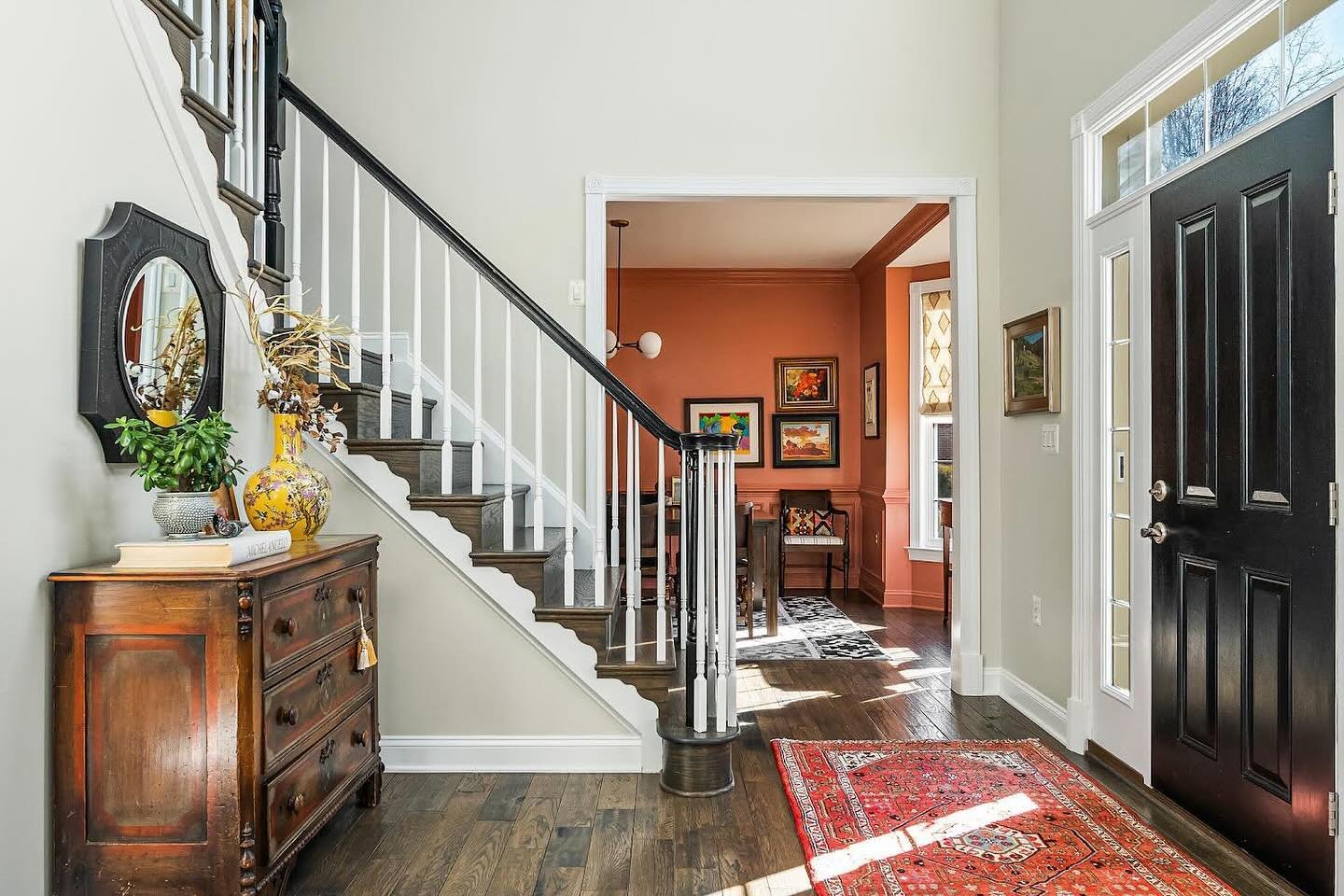 Creating a balanced color palette can be tricky. Here we paired creamy neutral walls in the common spaces juxtaposed with salmon walls in the adjacent dining room. Layering in a complimentary rug in the foyer, black accents on the door and mirror, an