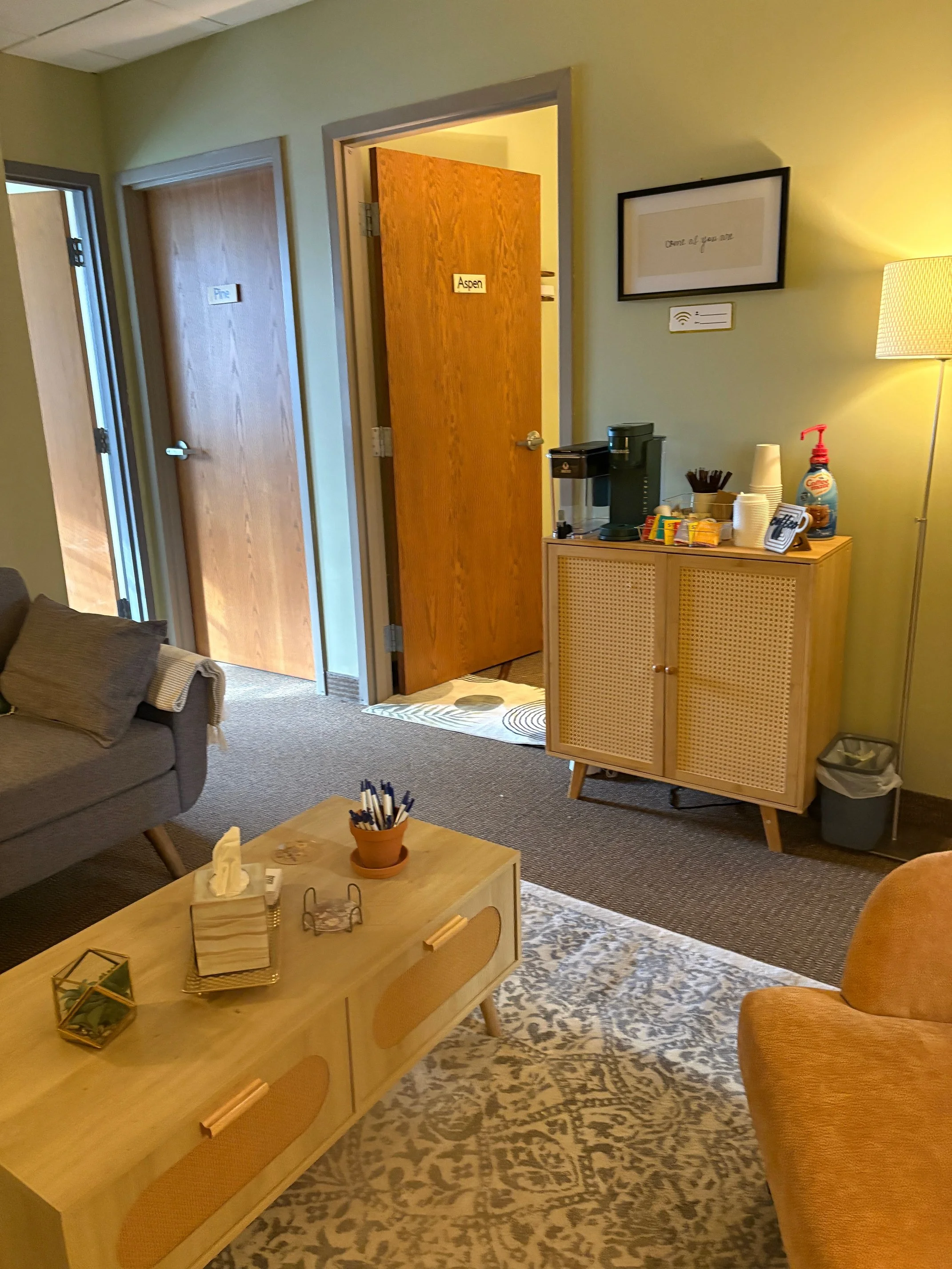 Hotel living room with a coffee table, couch, armchair, and a coffee station on a cabinet near the wall.
