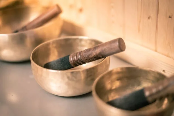 Three brass singing bowls with wooden mallets resting on top, placed on a wooden surface.