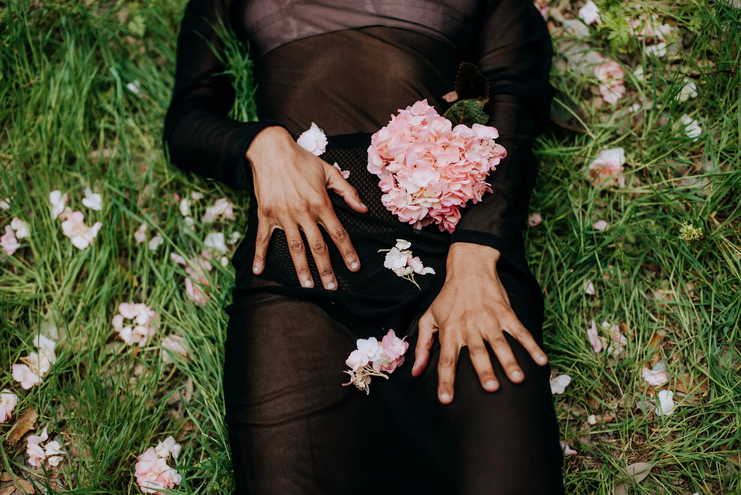 Nevan is laying in a field with pink flower petals on her dress