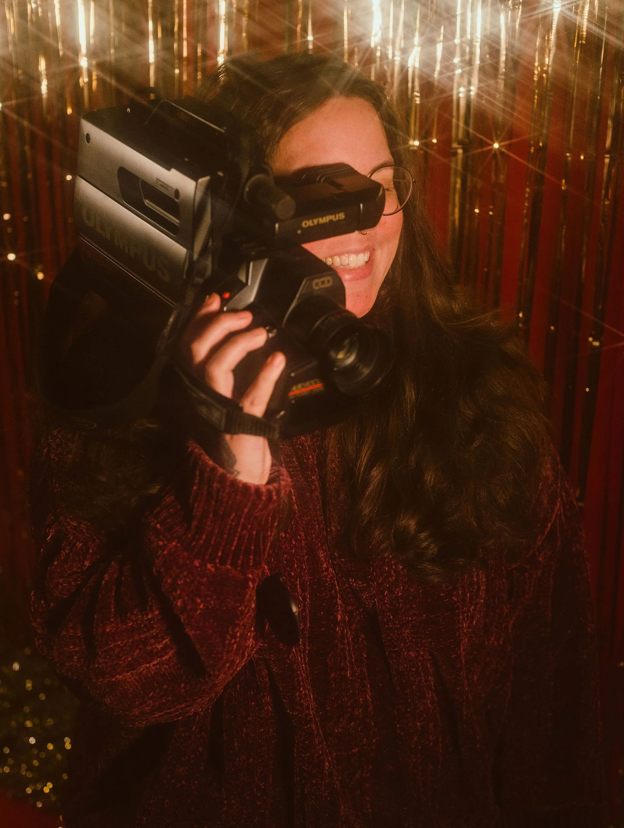 self portrait of danika taken in a vintage and retro style. they are holding a VHS camcoder and smiling.