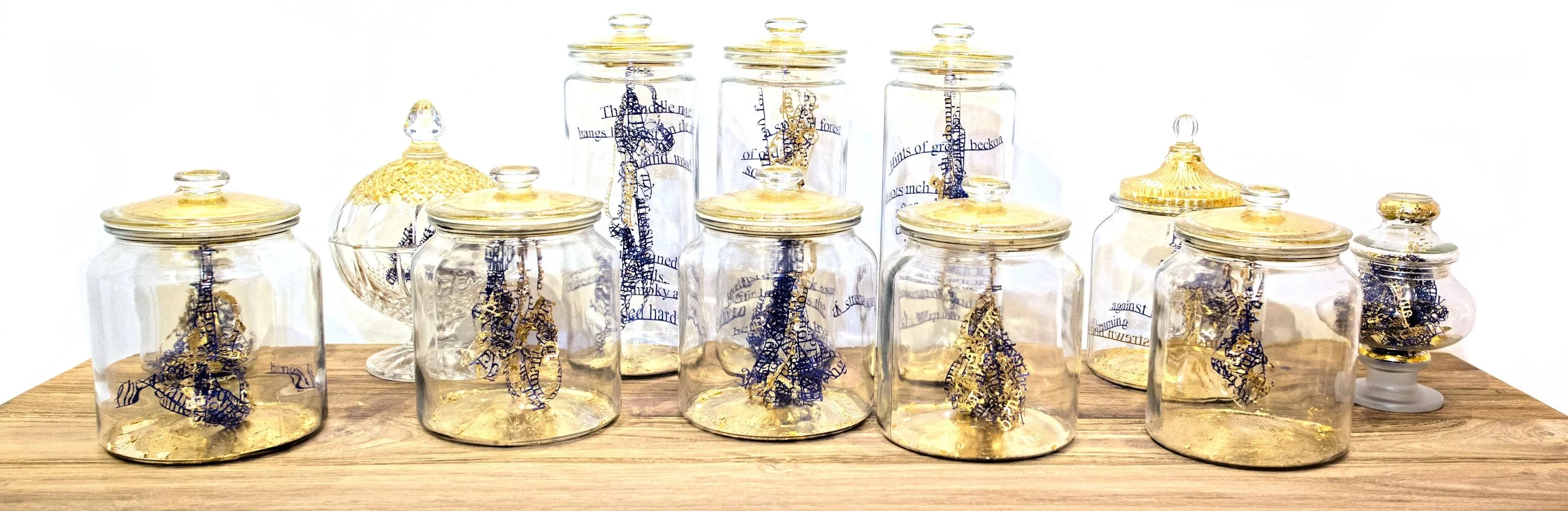 Twelve glass jars sit atop a wooden display piece, all capped with the familiar gold embellishment that seems to be a recurring artwork visual in the exhibition. As you move closer to this wooden table display, you catch a faint but lasting whiff of earthy scents, or Oudh – a delicate fragrance familiar to Kampong Glam.