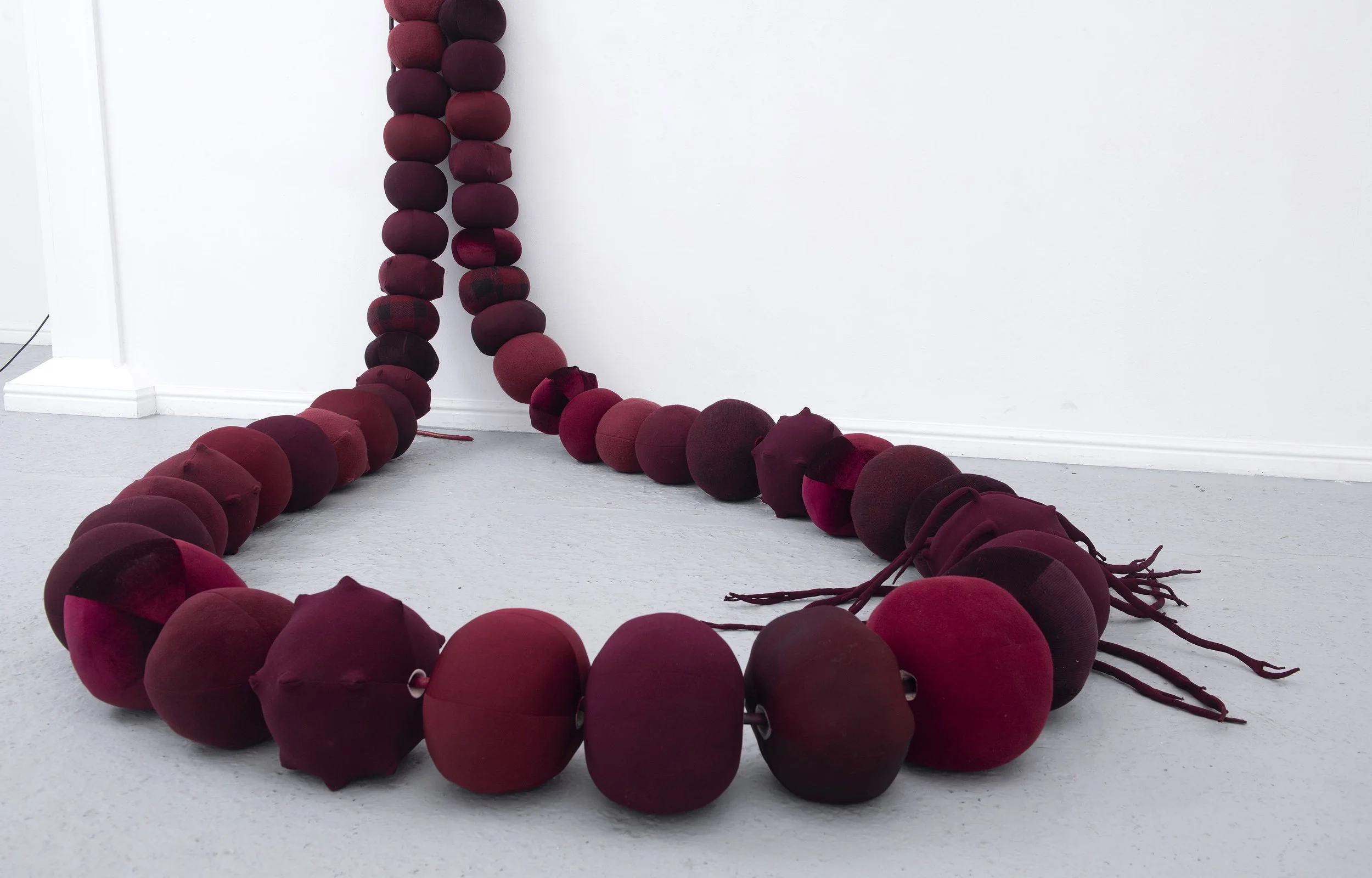   Beadwork: dealing with the leavings , 2025  49 repurposed hollow fibre filled fabric beads, vinyl and shimmer satin cord, metal hook and screws; Approx 2 x 2 x 2.5m. Image credit: Justin Piperger 