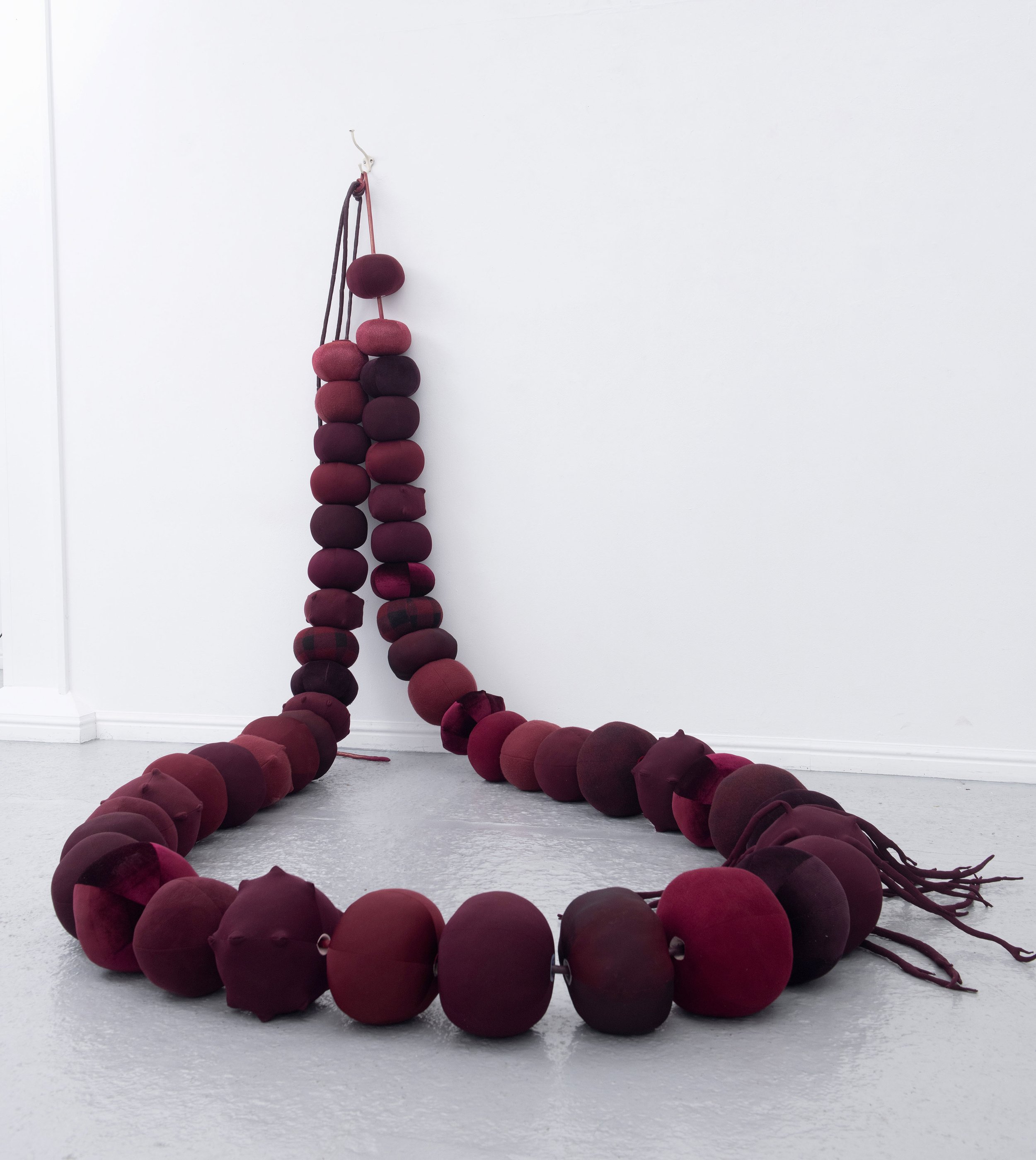   Beadwork: dealing with the leavings , 2025,  49 repurposed hollow fibre filled fabric beads, vinyl and shimmer satin cord, metal hook and screws; Approx 2 x 2 x 2.5m. Image credit: Justin Piperger     