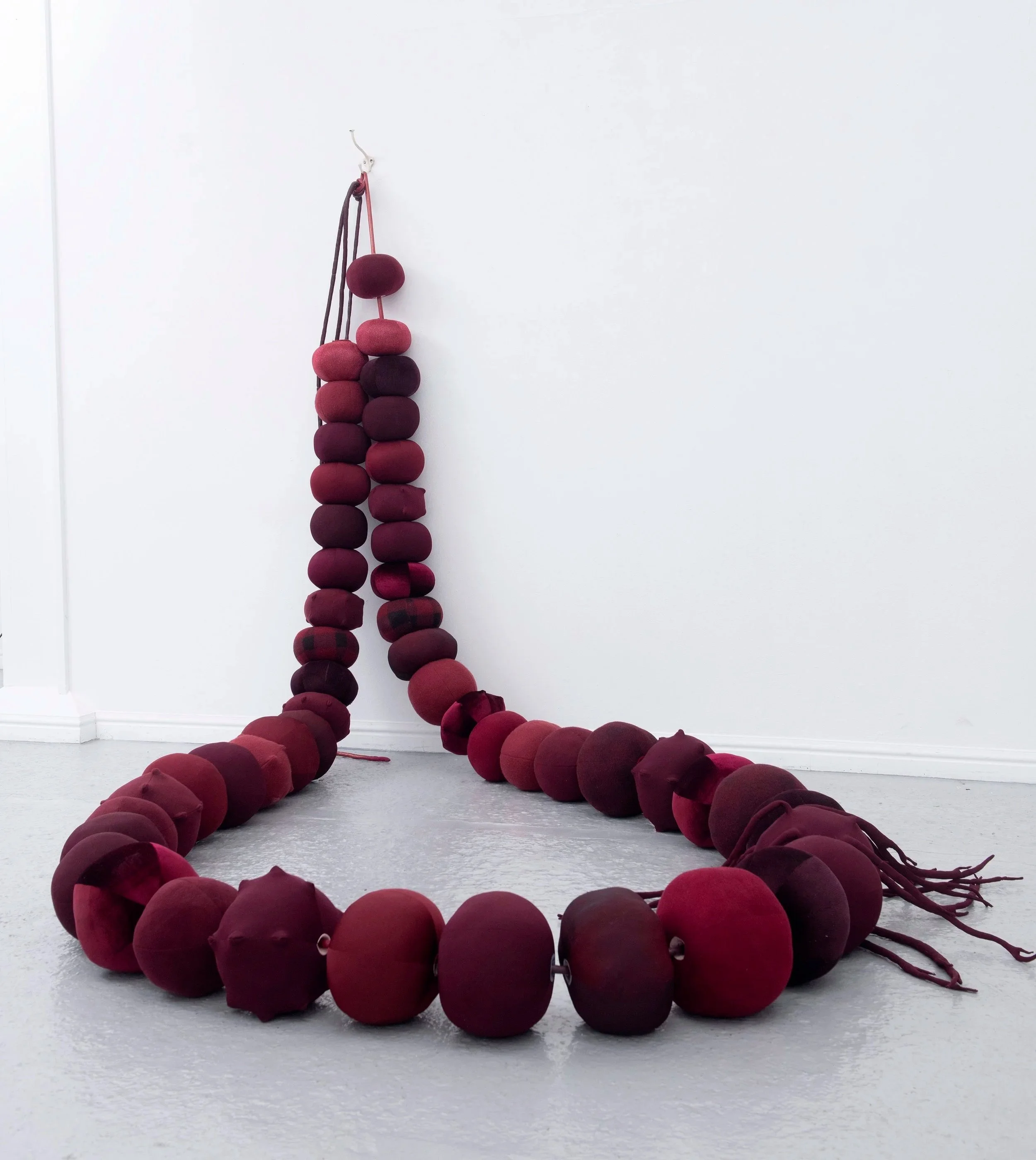   Beadwork: dealing with the leavings , 2025,  49 repurposed hollow fibre filled fabric beads, vinyl and shimmer satin cord, metal hook and screws; Approx 2 x 2 x 2.5m. Image credit: Justin Piperger     