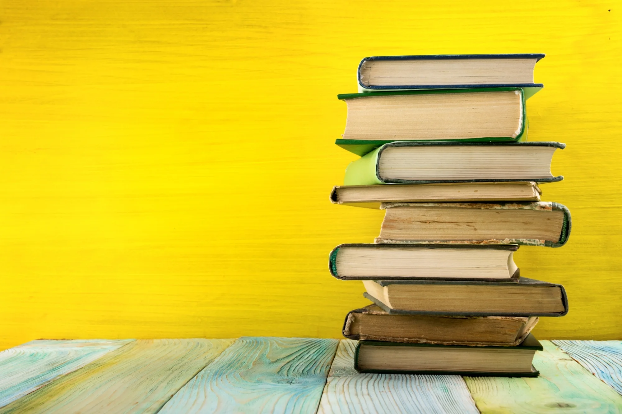 Stack of books, pages facing out on green table against yellow wall. Photo by Vimvertigo/iStock /Getty Images