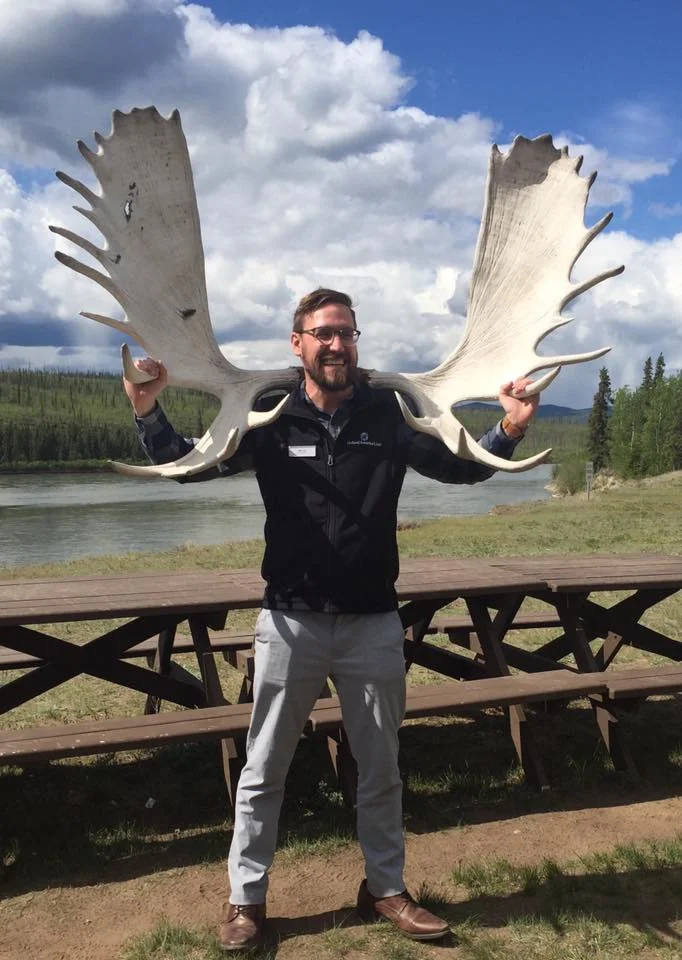 Jake is a tour guide in Alaska. He he poses with a pair of moose antlers.