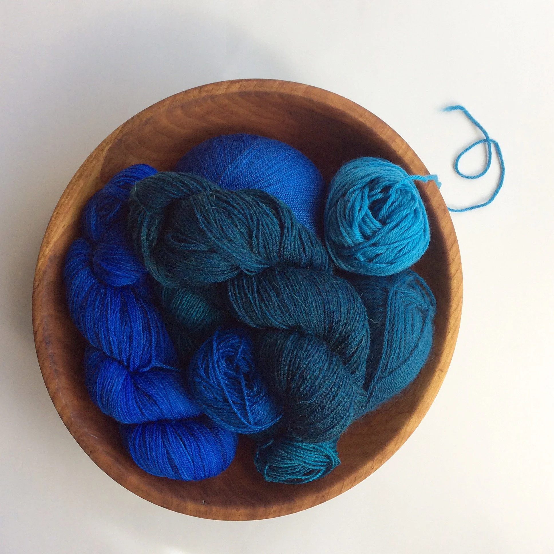 skeins of blue and teal yarn in a wooden bowl