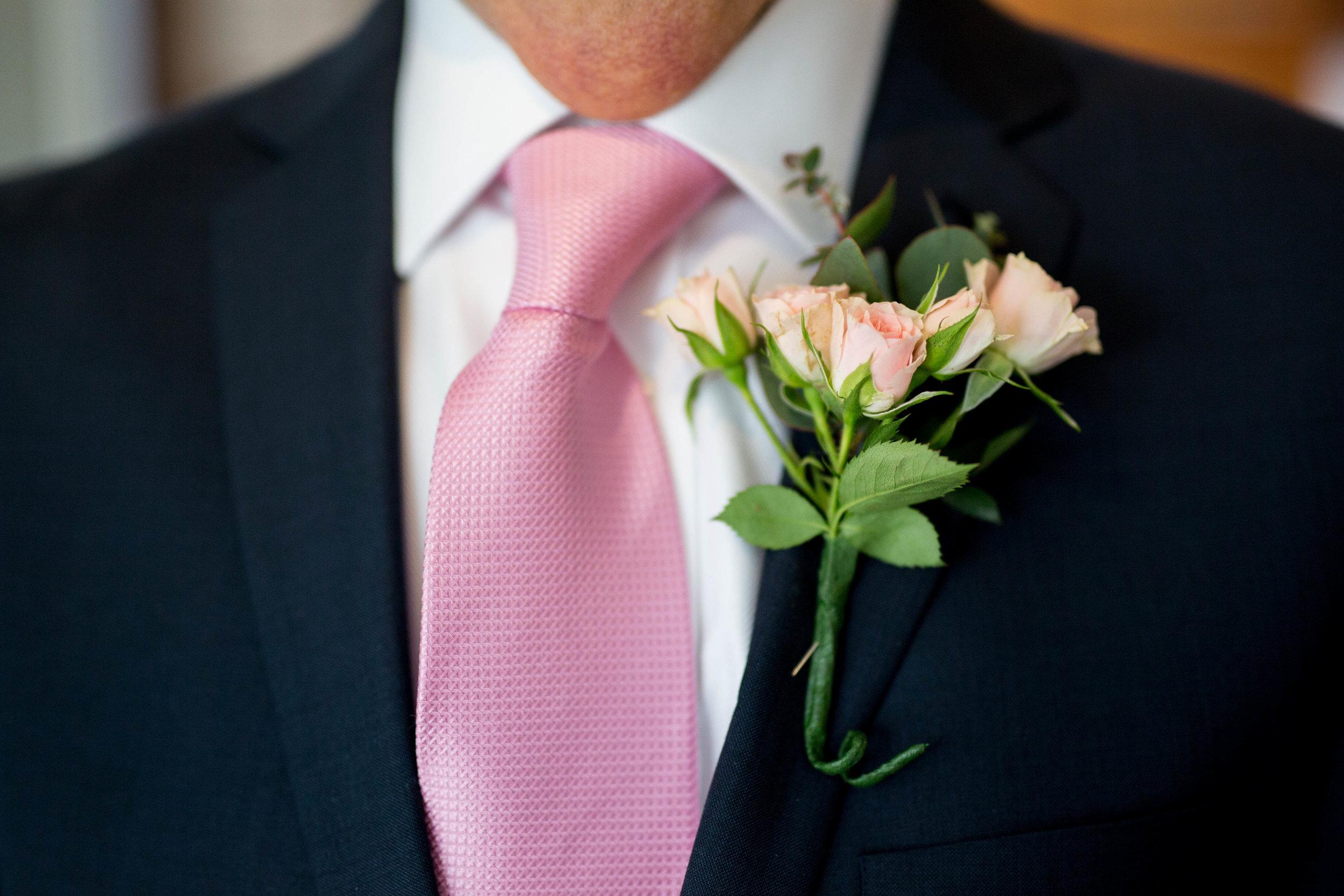 Close-up of a man wearing a suit with a pink tie and a boutonniere with pink roses.