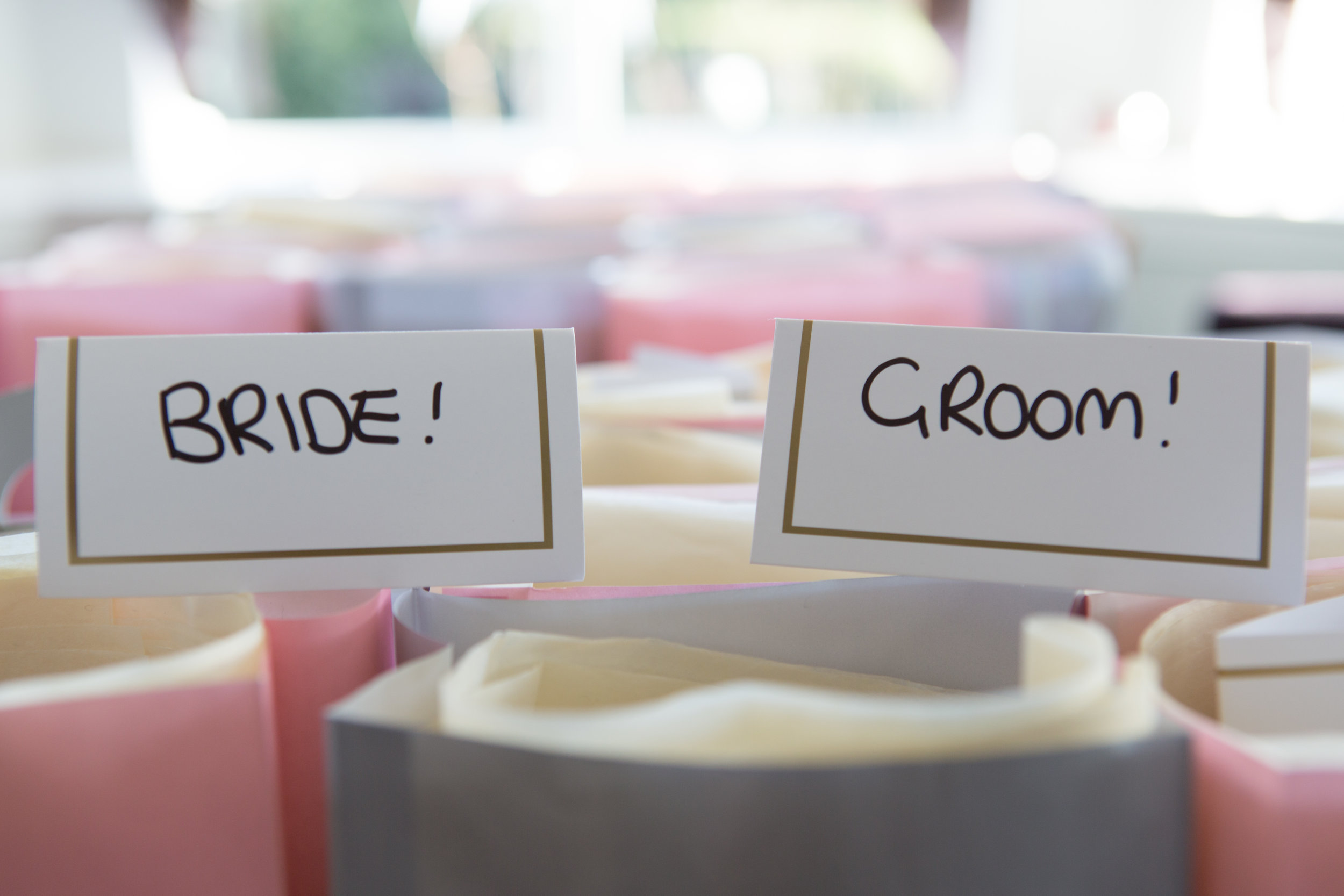 Place cards labeled "Bride!" and "Groom!" on top of gift bags with pink and white tissue paper.