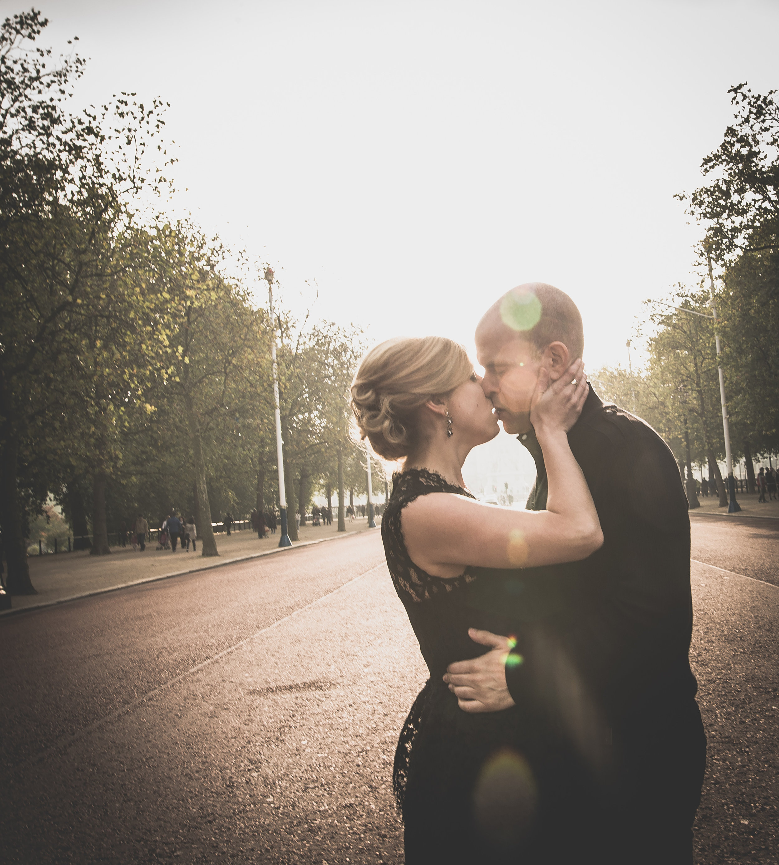 A couple kissing on an empty street with trees and a soft sunset glow.