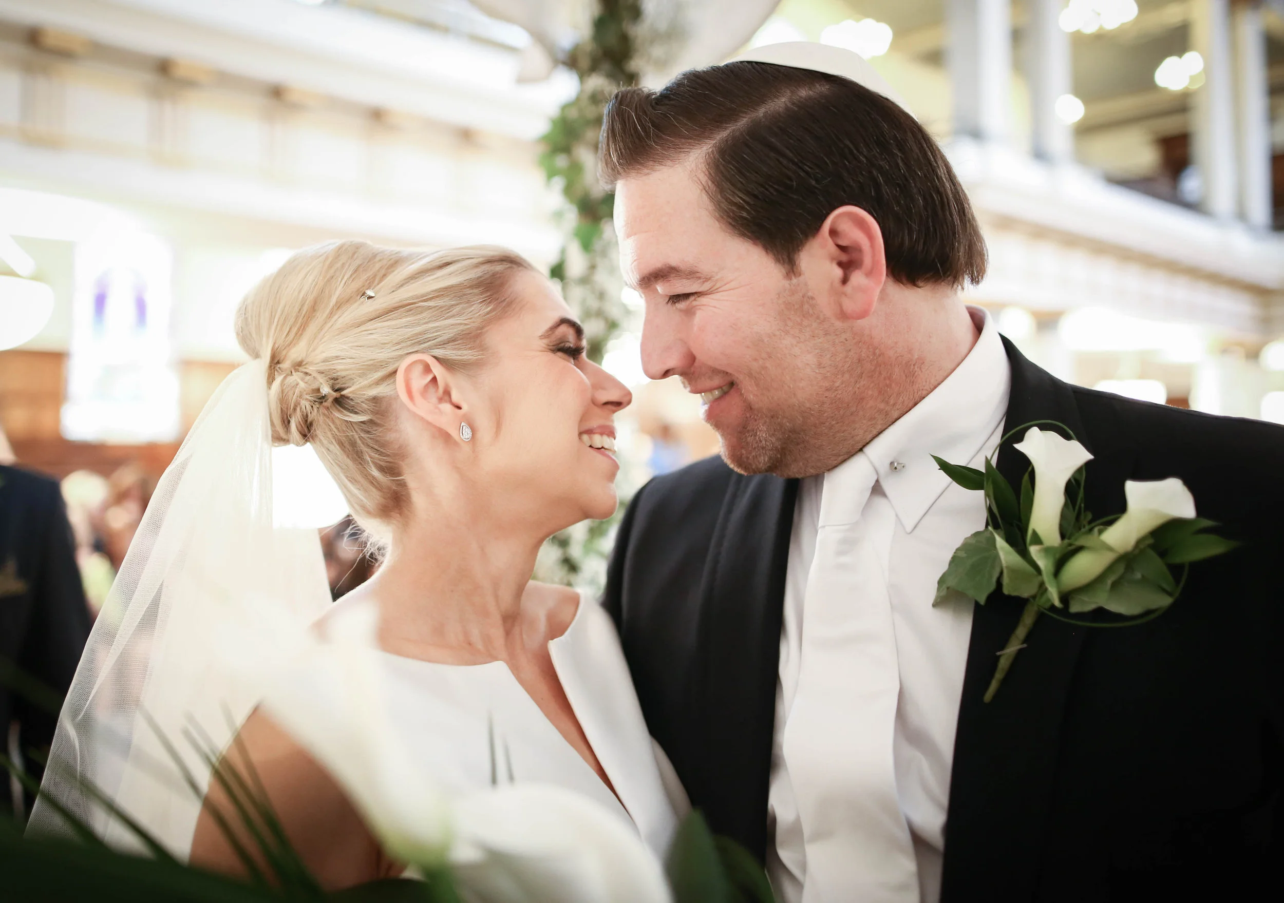 Bride and groom smiling at each other during wedding ceremony in a decorated venue.