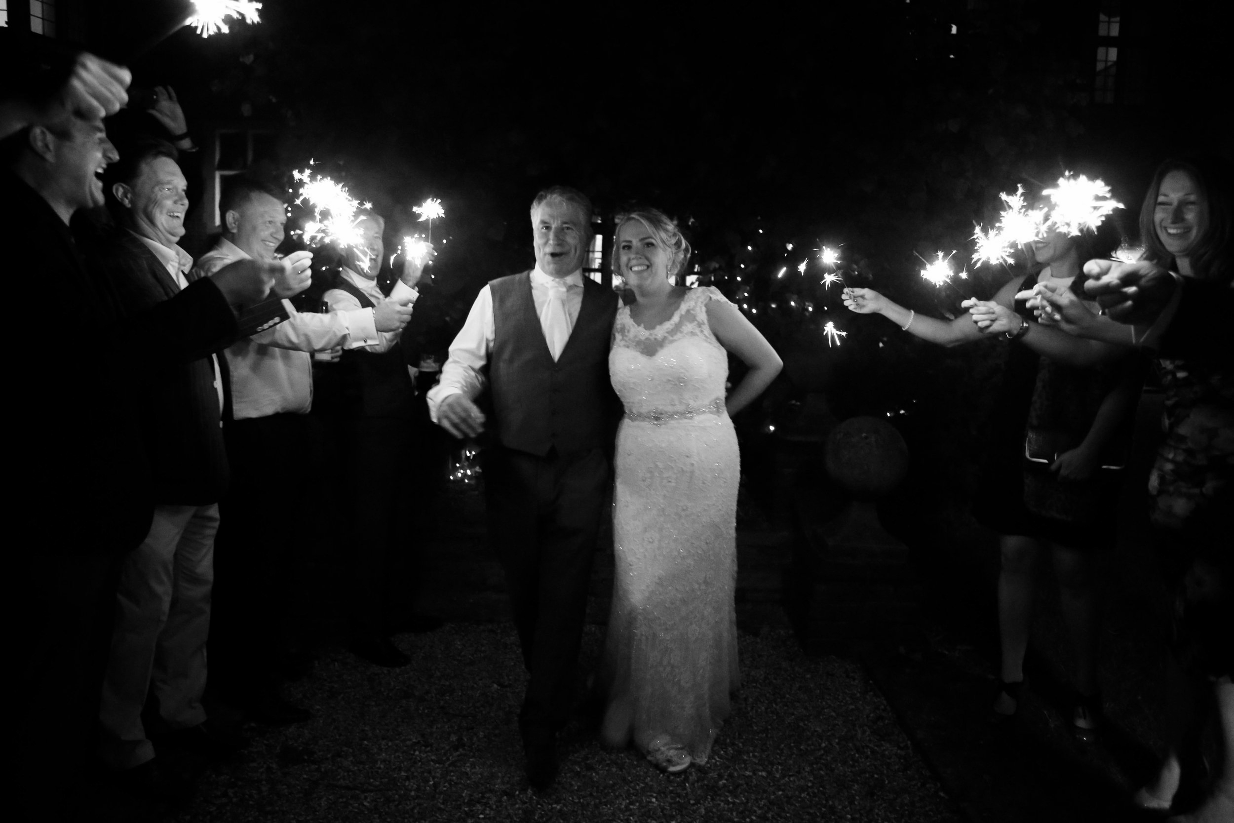 A bride and groom walking down a path surrounded by people holding sparklers at night.