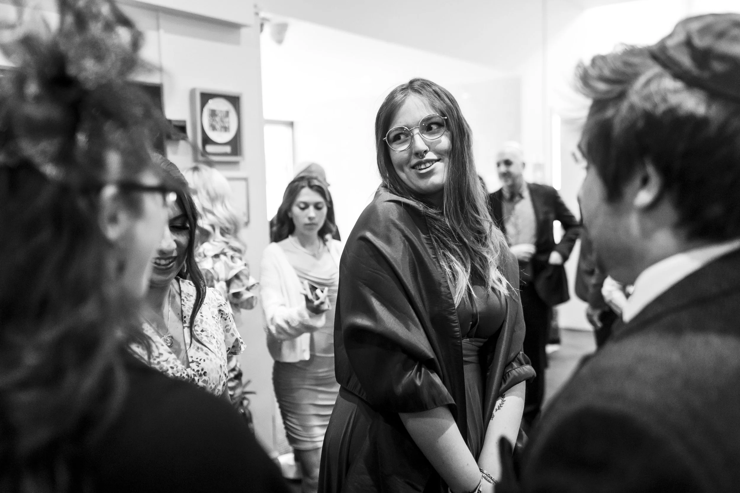Group of people socializing and smiling at an indoor event, black and white photo.