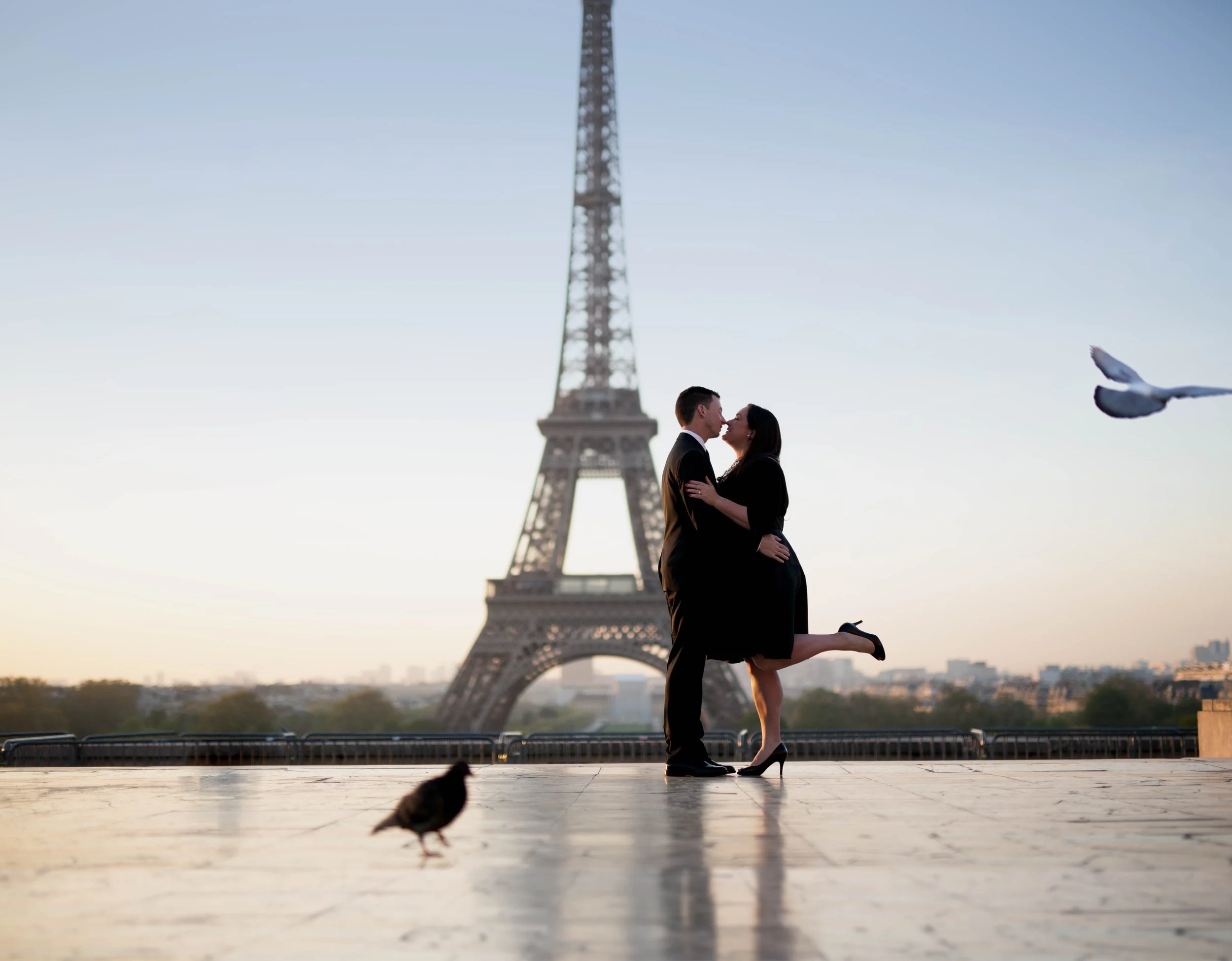 Couple kissing in front of Eiffel Tower in Paris, sunrise background, with pigeon and dove.