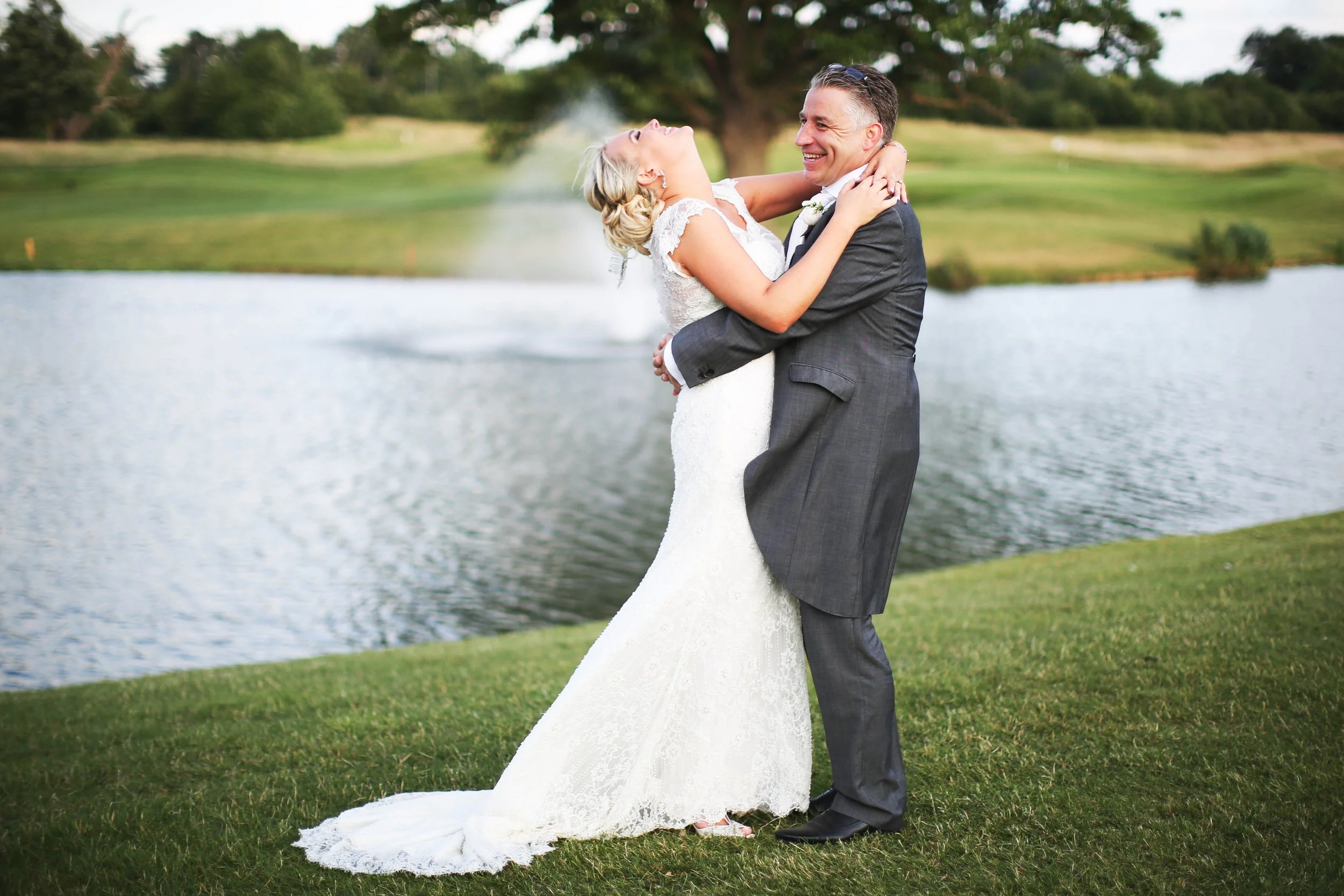 A bride and groom laughing near a lake on their wedding day.