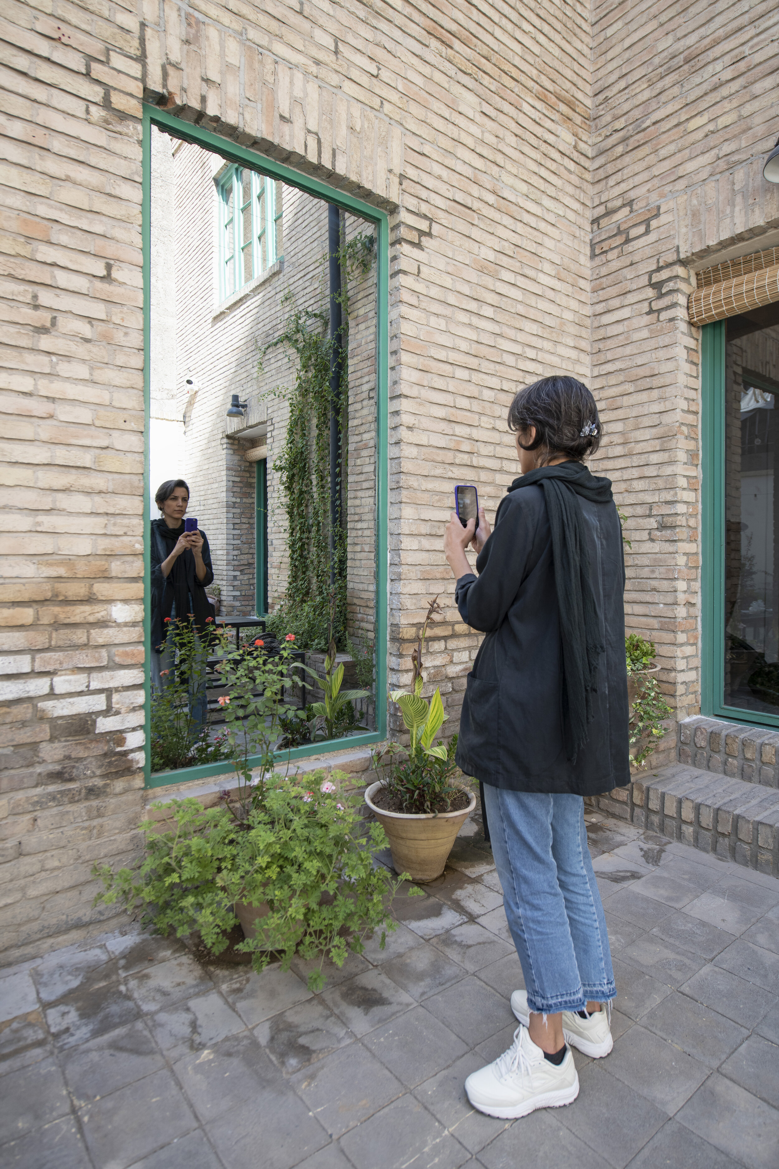  The courtyard view to: Untitled (One-way Mirror to the Communal Room)  One-way Mirror  230 x 109 CM (بدون عنوان (آینه یکطرفه به اطاق اشتراکی  * A visitor is looking into the mirror side of the “one-way mirror” and taking a selfie not realizing she i