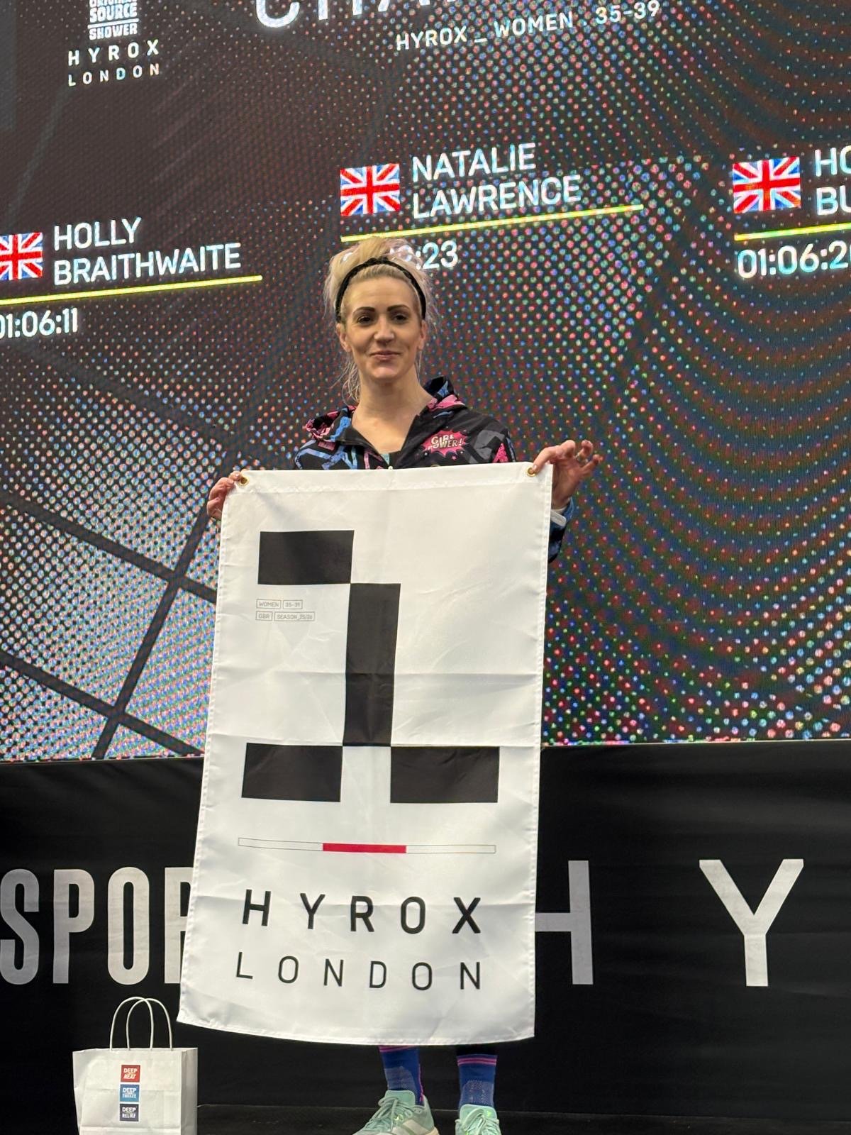 Nat Lawrence holding a HYROX London flag after winning the Women’s Pro race at London Olympia.