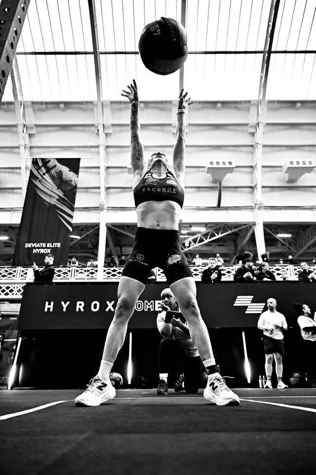 Black and white image of Nat Lawrence throwing a wall ball during a HYROX competition.
