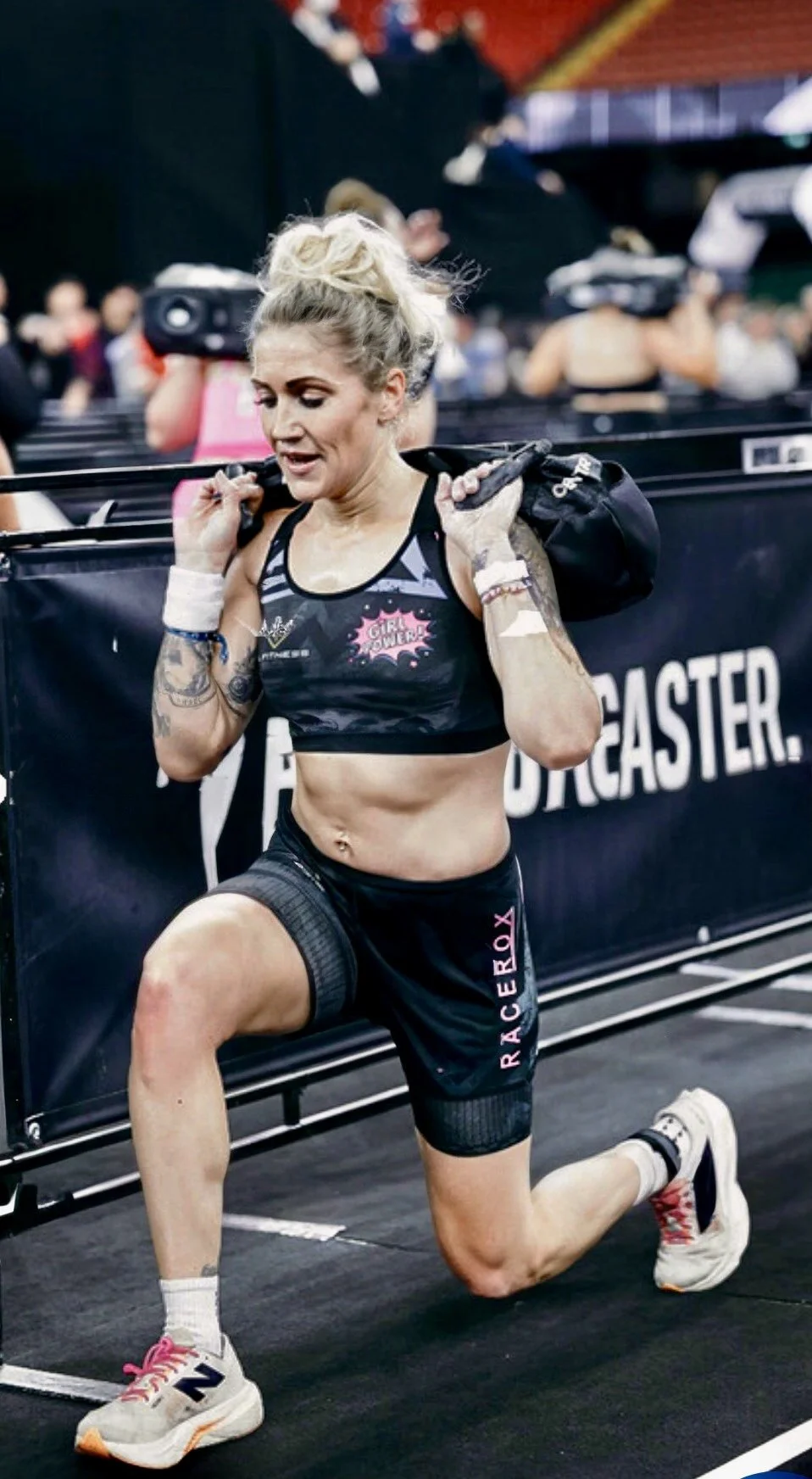 Nat Lawrence carrying a sandbag during a lunge station at a HYROX competition.