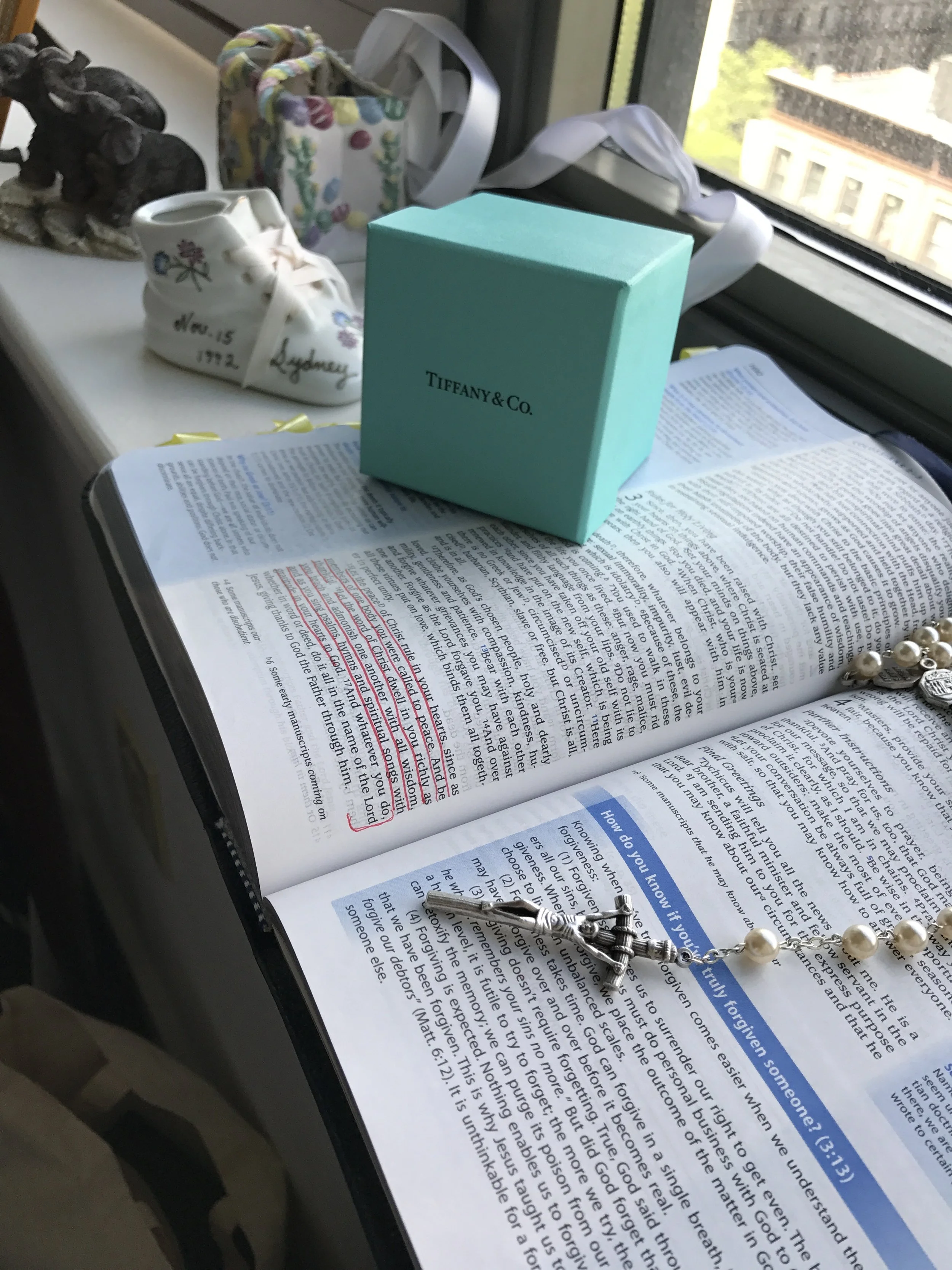 In the foreground is my Rosary, laid atop my Bible with our wedding verses underlined in red. Beyond that, our wedding bands from Tiffany + Co. Further still is the little ceramic shoe gifted to my parents upon my birth, with my name, birthdate, weight and length on it. 