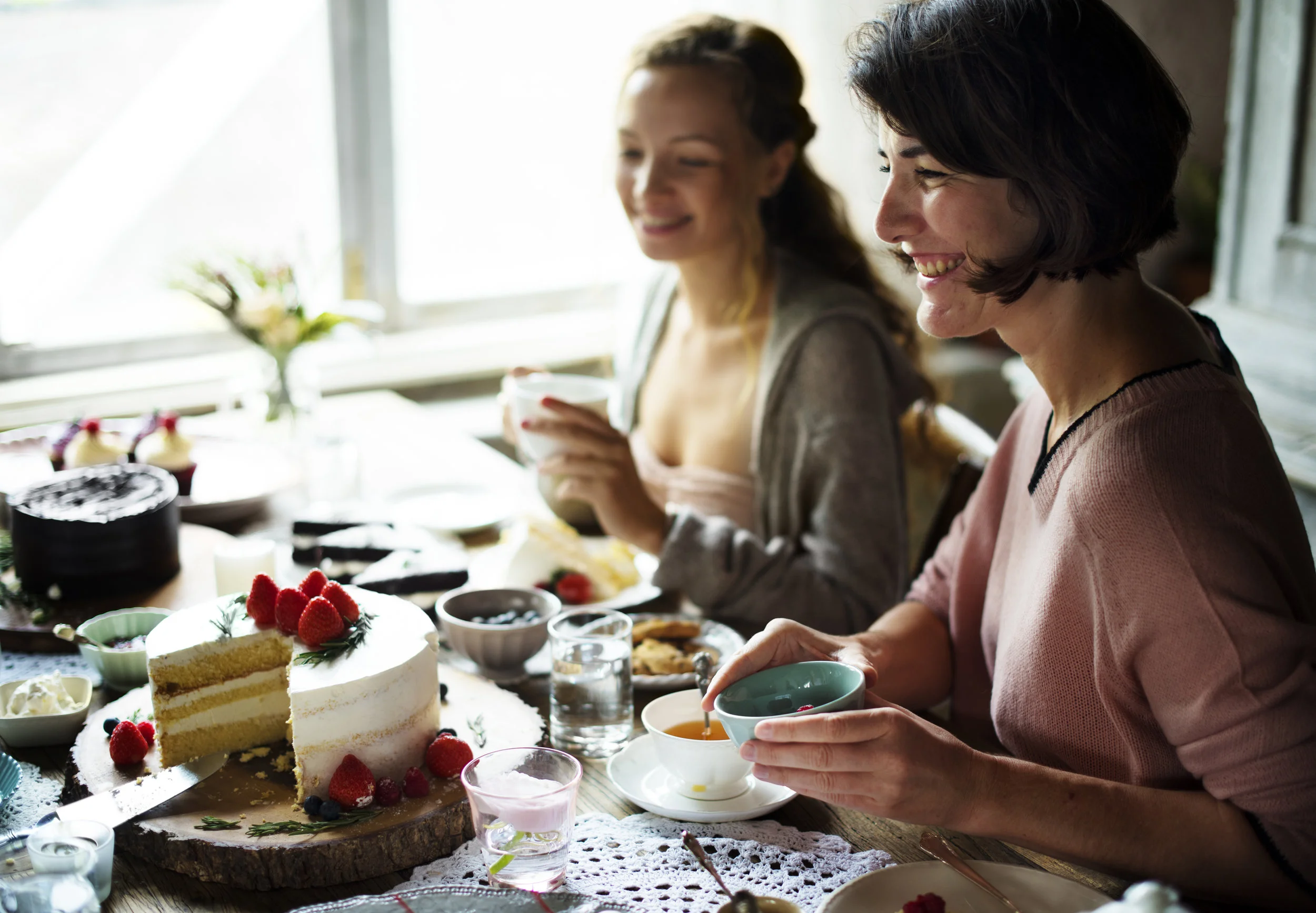 Two women drinking tea sitting at a table with cakes