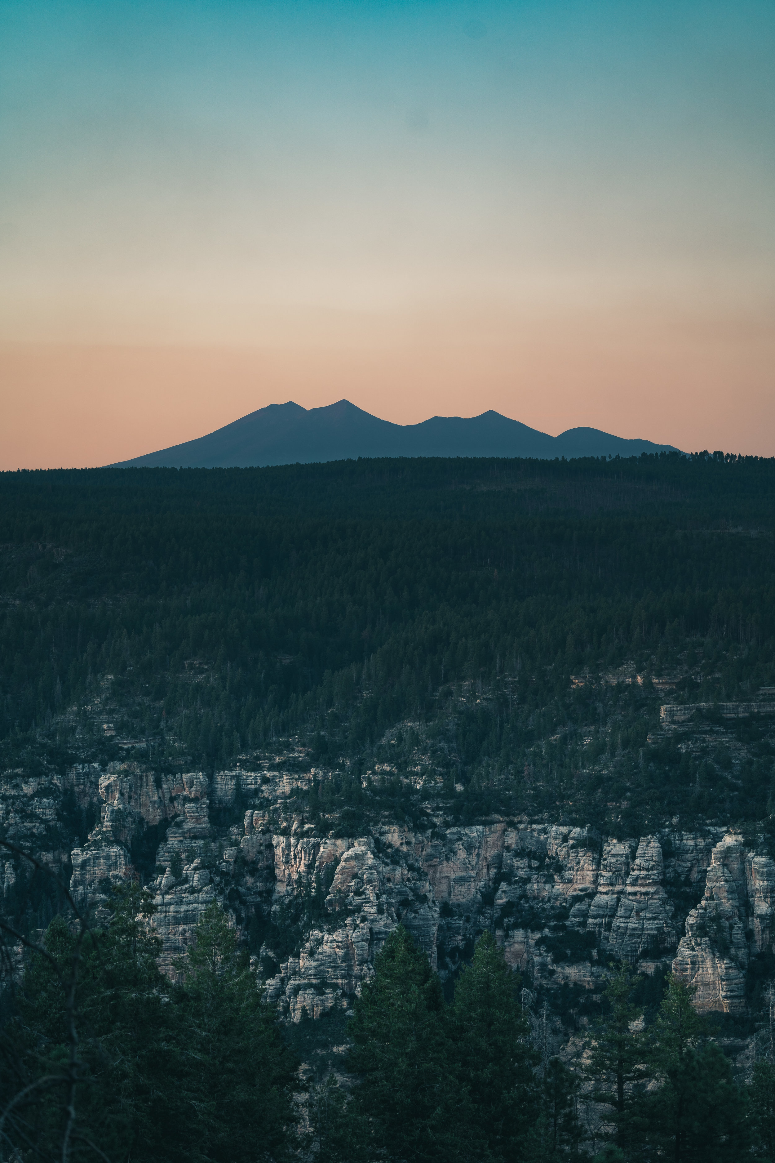 The West Fork of Oak Creek Canyon tears into the Colorado Plateau in the foreground, while San Francisco Mountain is silhouetted against the orange and teal twilight.