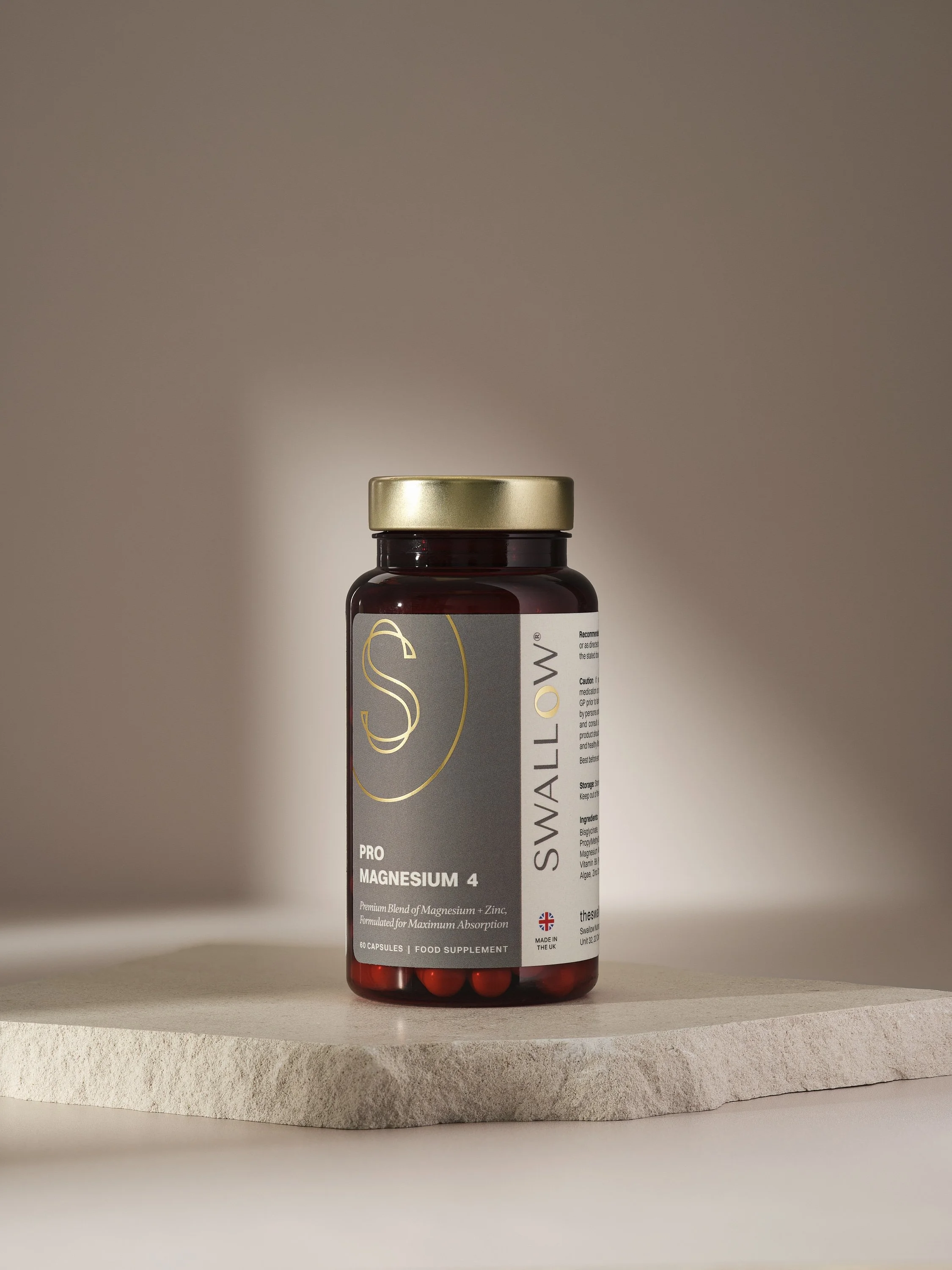 Bottle of Swallow Pro Magnesium 4 dietary supplements with capsules inside, placed on a stone slab against a neutral background.