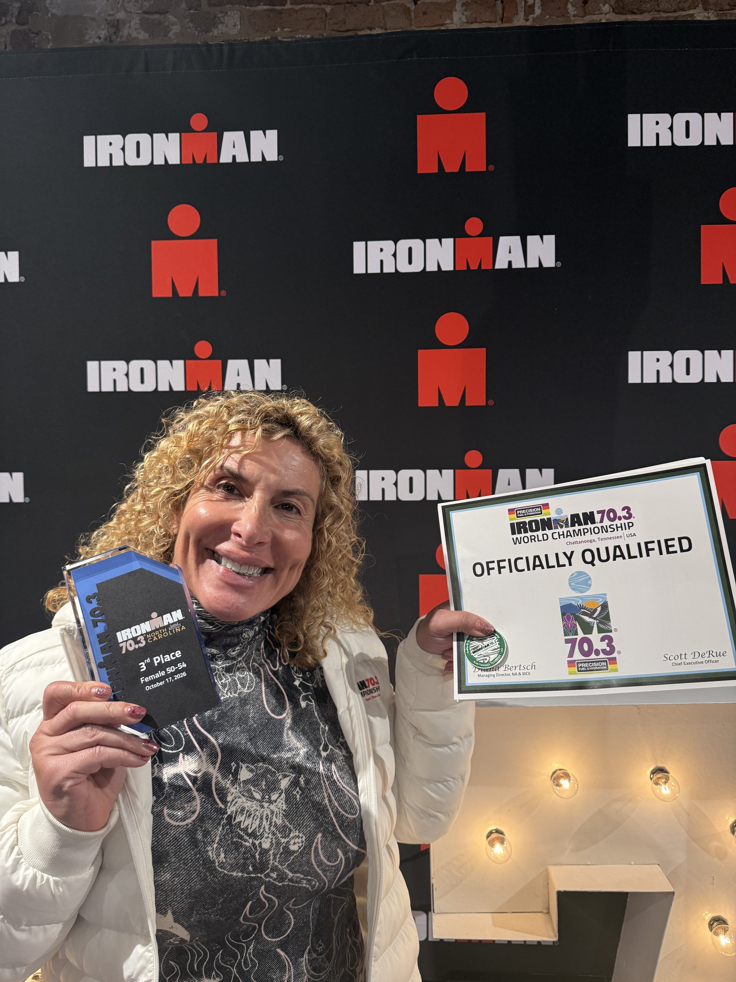 ForzaFit coach Rosa Laura proudly holding her third-place age-group award, World Championship qualification certificate, and coin at IRONMAN 70.3 North Carolina 2026, qualifying for Chattanooga 2027.