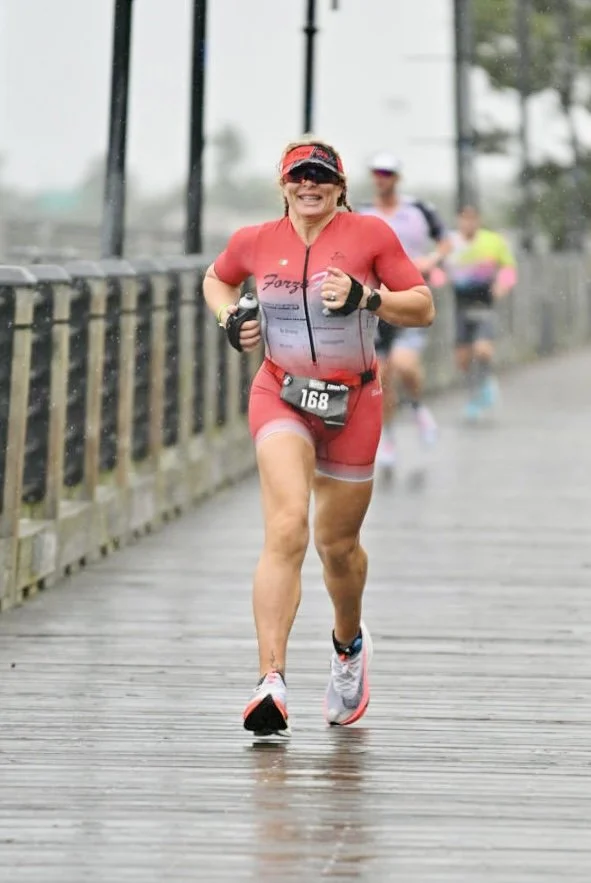 ForzaFit triathlete Rosa Laura smiling while running on a wet boardwalk during IRONMAN 70.3 North Carolina.