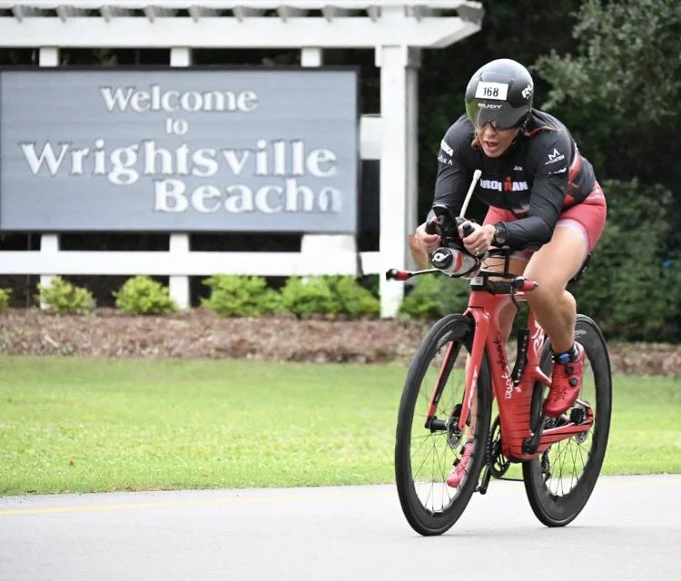 Rosa Laura of ForzaFit racing past the Welcome to Wrightsville Beach sign at IRONMAN 70.3 North Carolina 2026, earning the fastest bike split in her age group.