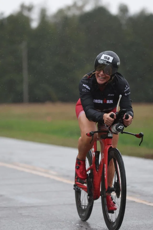 ForzaFit coach Rosa Laura cycling through heavy rain on wet roads during IRONMAN 70.3 North Carolina 2026.