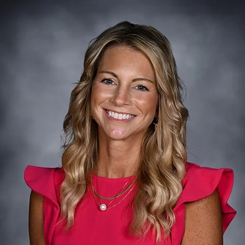 Smiling woman with long blonde hair, wearing a black top and necklace, against a gray background.